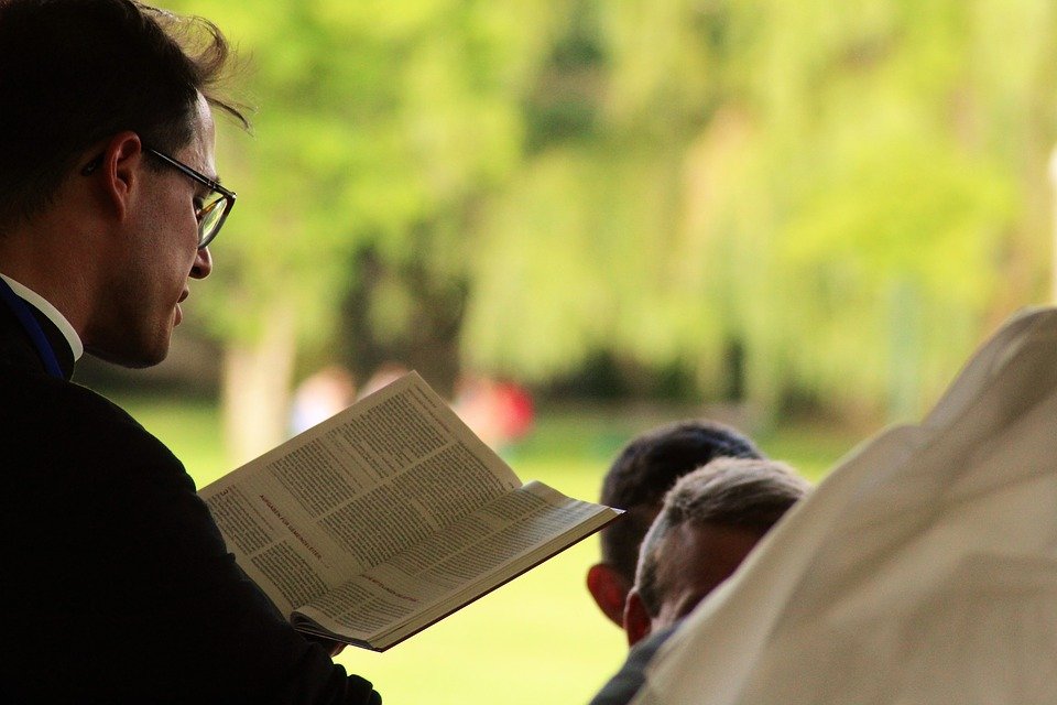 A priest reads from a book during a church meeting | Photo: Pixabay