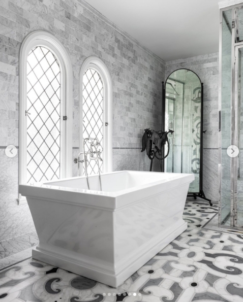 One of the estate's 11 bathrooms is finished entirely in grey marble, from the brick-laid wall tiles to the patterned floor beneath a freestanding white soaking tub. Diamond-paned leaded windows filter the light above the bath, whilst a tall arched mirror and an ornately etched glass shower screen complete a space that feels closer to a European spa than a private residence. | Source: Instagram/top.music.songs