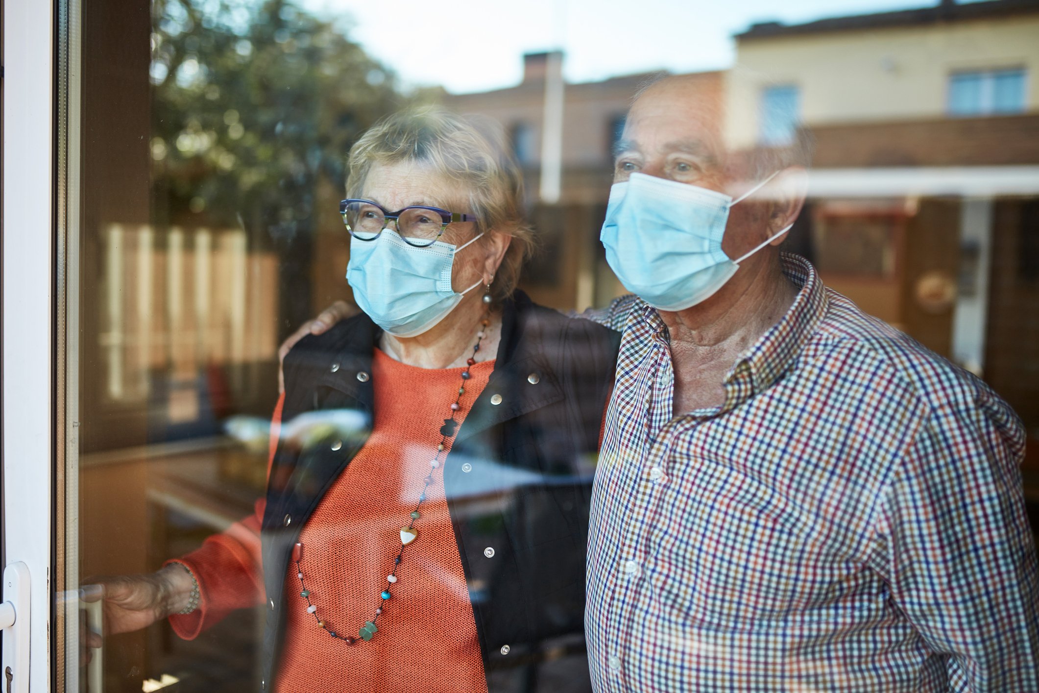 Beispielhaftes Bild eines besorgten älteren Paares, das mit Masken aus dem Fenster schaut | Quelle: Getty Images