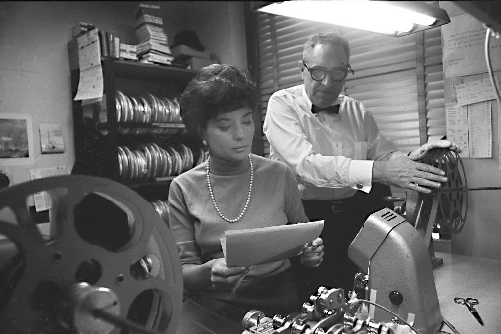 American broadcast journalist Barbara Walters reviews a script as an unidentified man threads a projector at NBC Studios, New York, New York, 1966. | Source: Getty Images