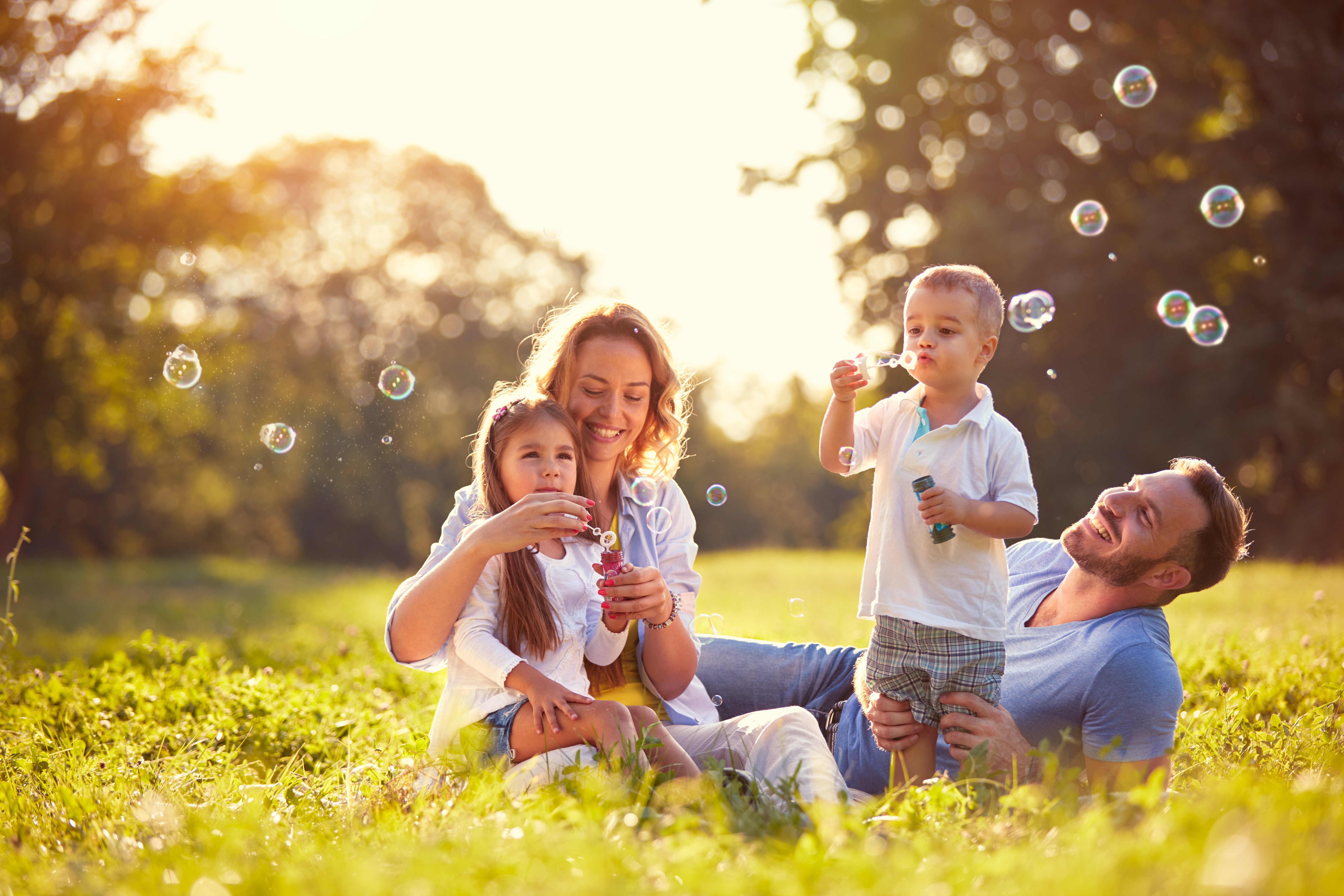 Una familia feliz haciendo burbujas sentada sobre el pasto. | Foto: Shutterstock