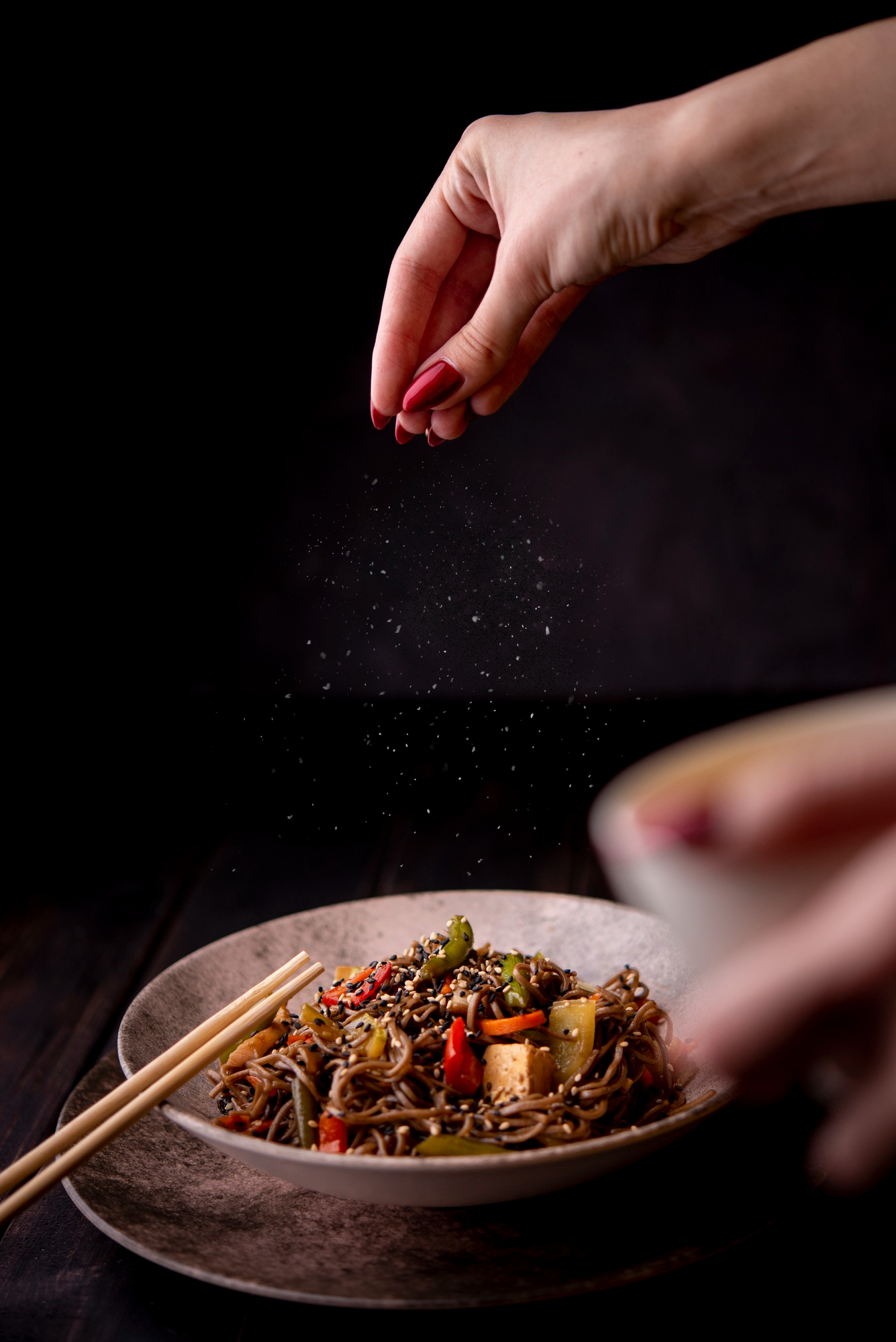 A woman sprinkling salt in a bowl of noodles | Source: Freepik