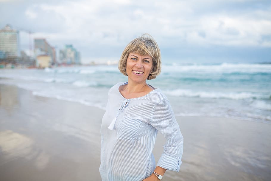 Mujer sonriendo mientras posa con una playa en el fondo. | Foto: PxFuel