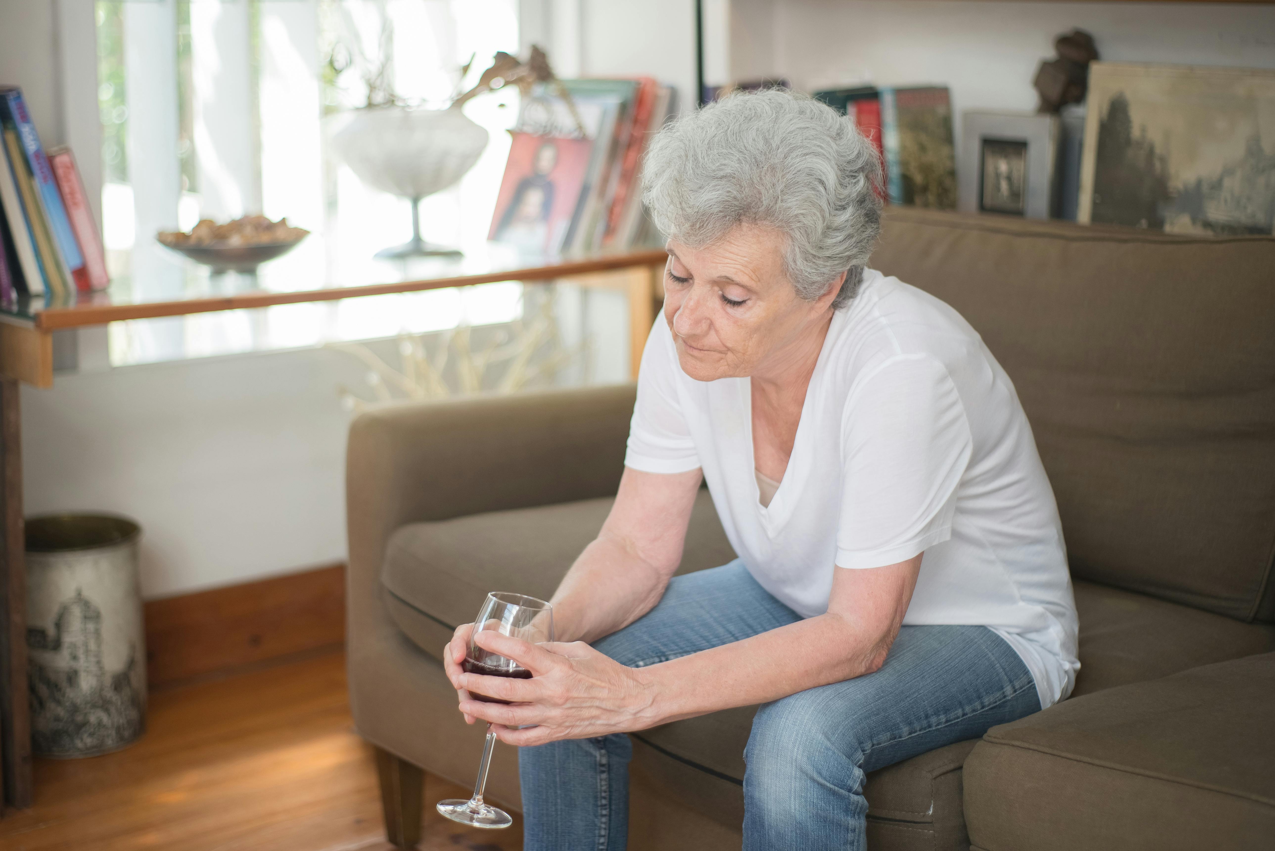 A sad-looking woman drinking a beverage while seated on a couch | Source: Pexels