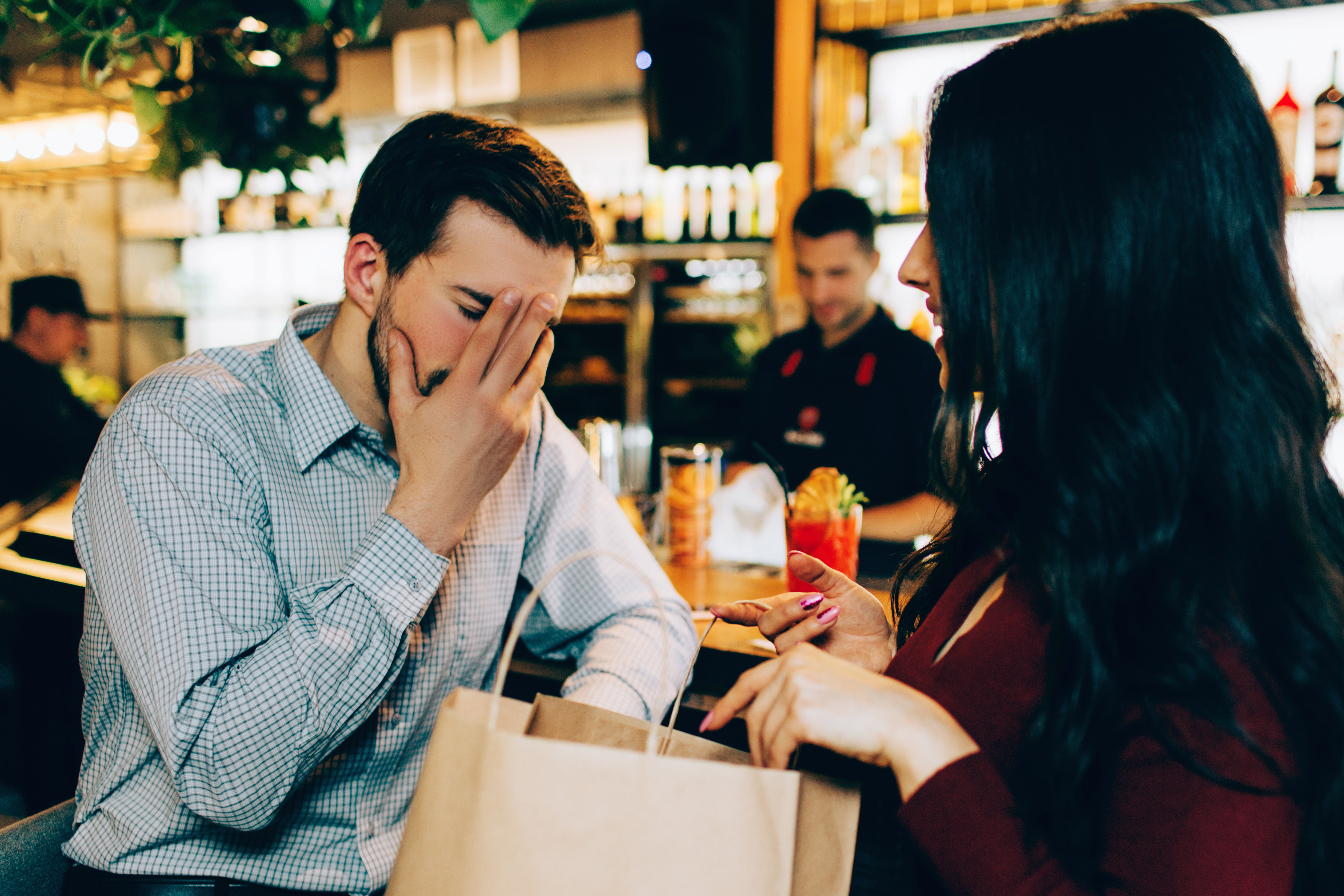 A man looking displeased with his hand on his face while talking to a woman at a restaurant | Source: Shutterstock