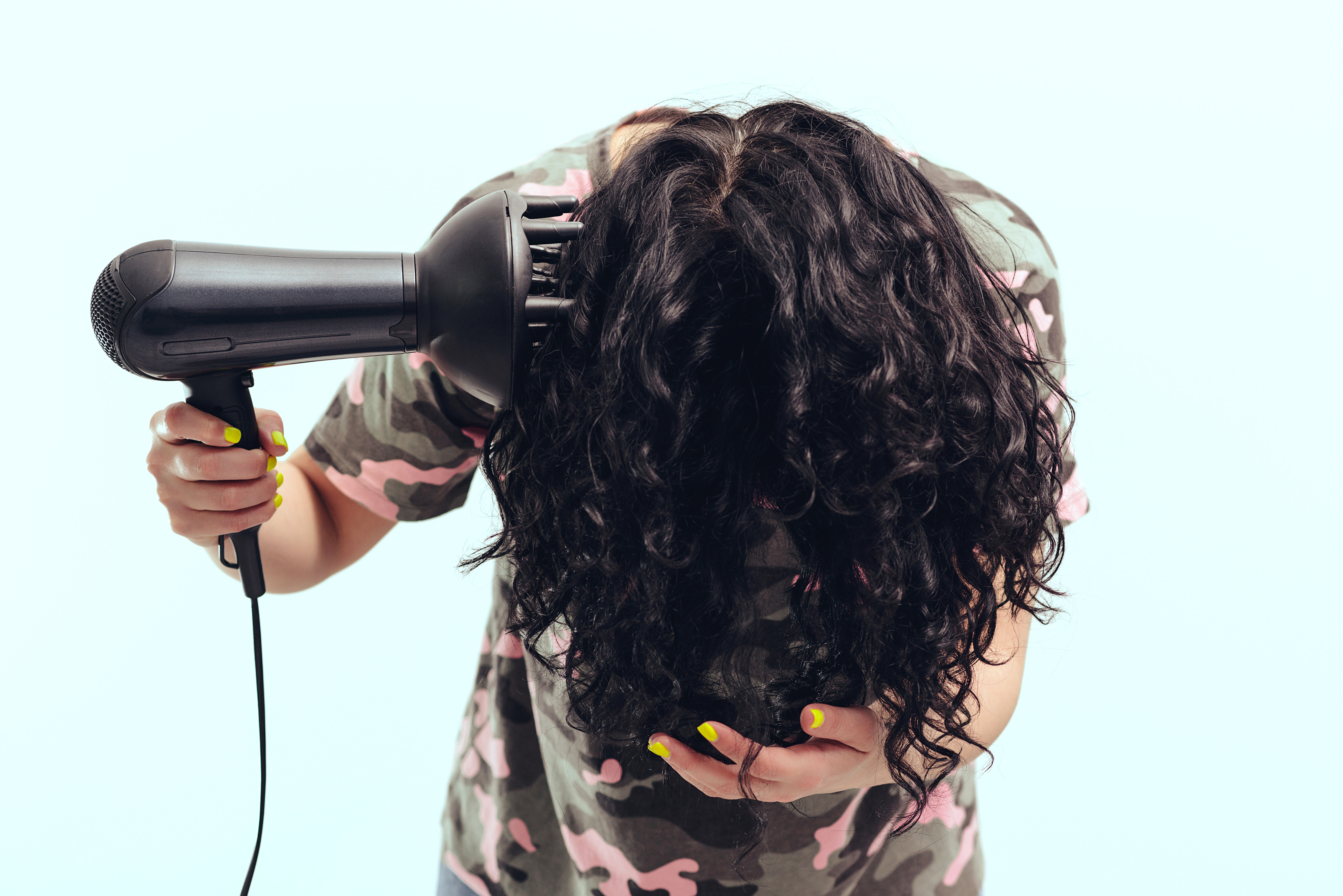 A woman is pictured styling her curly hair with hairdryer with special diffuser nozzle | Source: Shutterstock