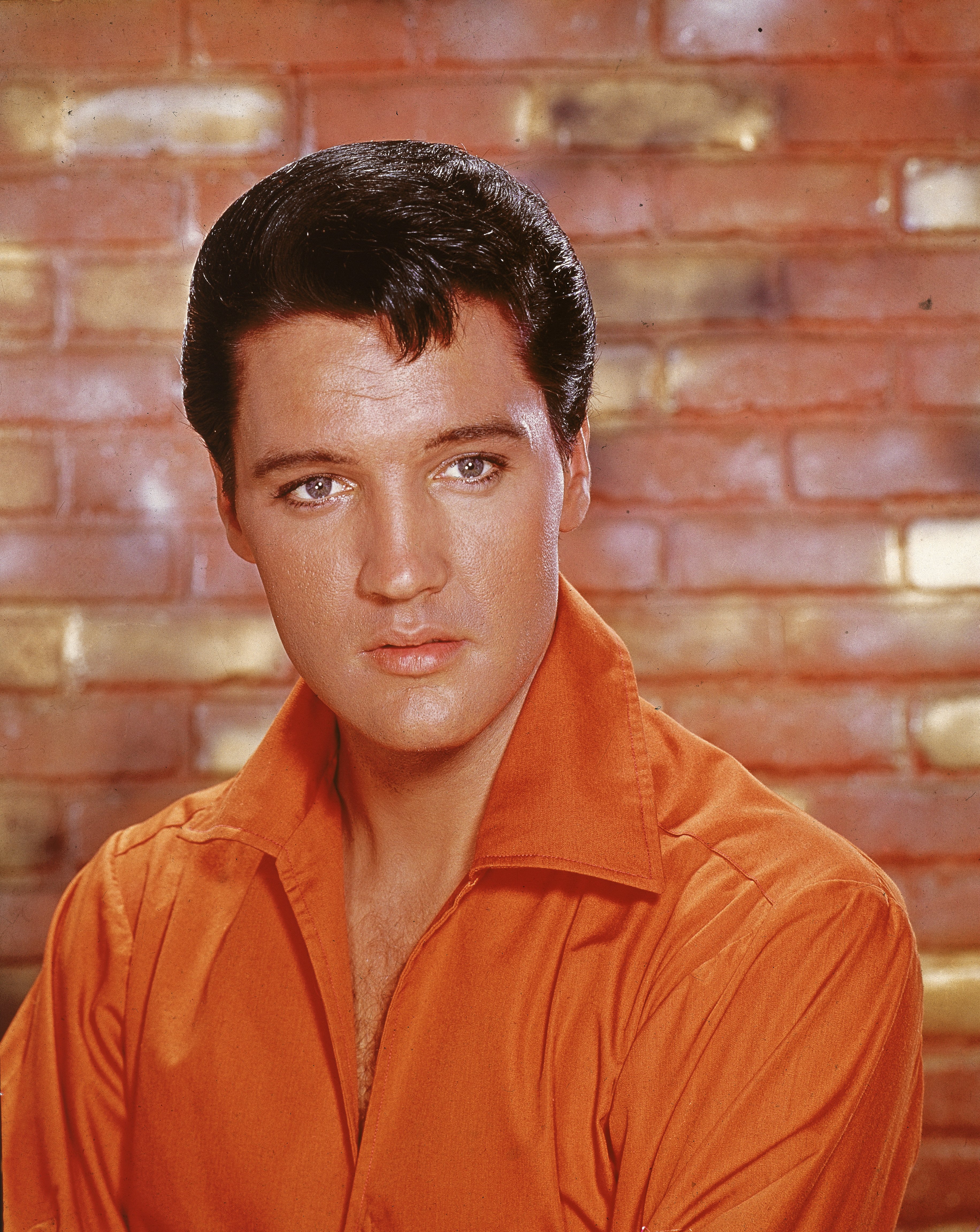 Portrait of American rock and roll singer Elvis Presley, dressed in an orange open-neck shirt and in front of a brick wall, mid 1960s | Source: Getty Images