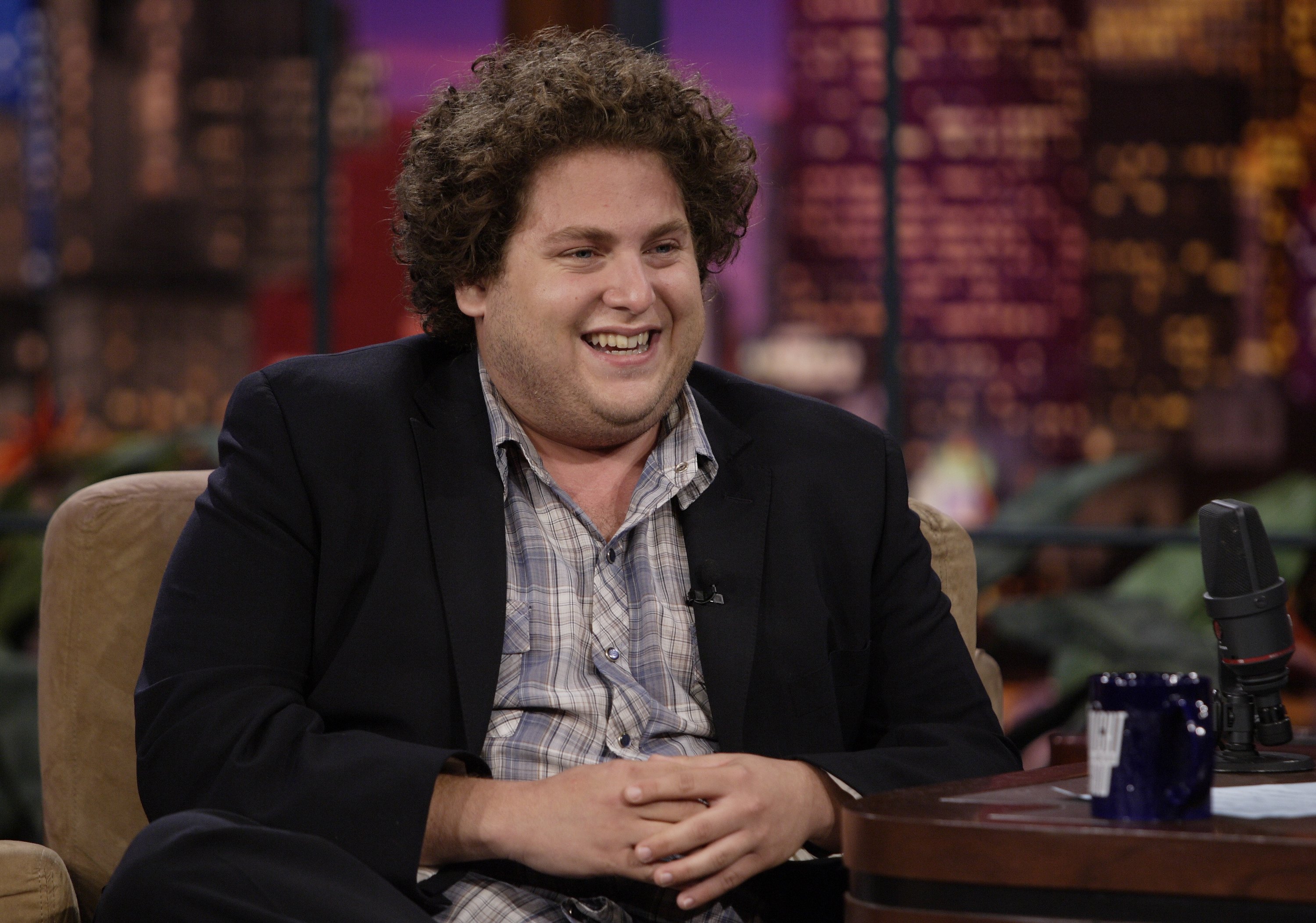 Jonah Hill flashed a wide smile during an appearance on "The Tonight Show with Jay Leno" on August 8, 2007, the same year "Superbad" propelled him into the Hollywood spotlight. With his full cheeks and thick brown curls framing his face, the then-23-year-old actor displayed the youthful look that became closely associated with his breakout era — and would later stand in striking contrast to his transformation in the years ahead.