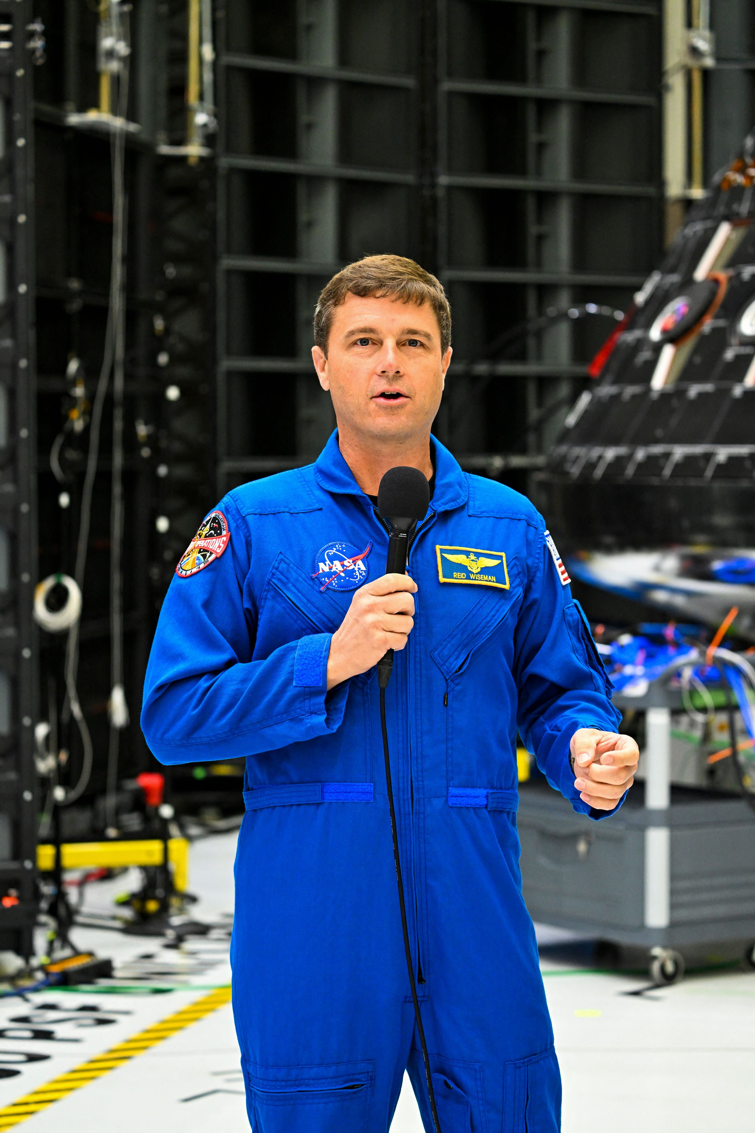 US astronaut Reid Wiseman, commander, speaks in front of the Artemis II crew module (rear) inside the Neil Armstrong Operations and Checkout Building at the Kennedy Space Center in Cape Canaveral, Florida, on August 8, 2023. | Source: Getty Images