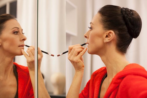 Une femme se maquillant devant un miroir. | Photo : Getty Images