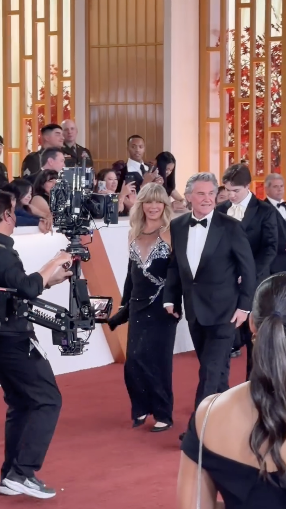Goldie Hawn glances back over her shoulder while walking beside Kurt Russell, with the iconic Oscars statue visible near the red carpet entrance. | Source: Instagram/enews