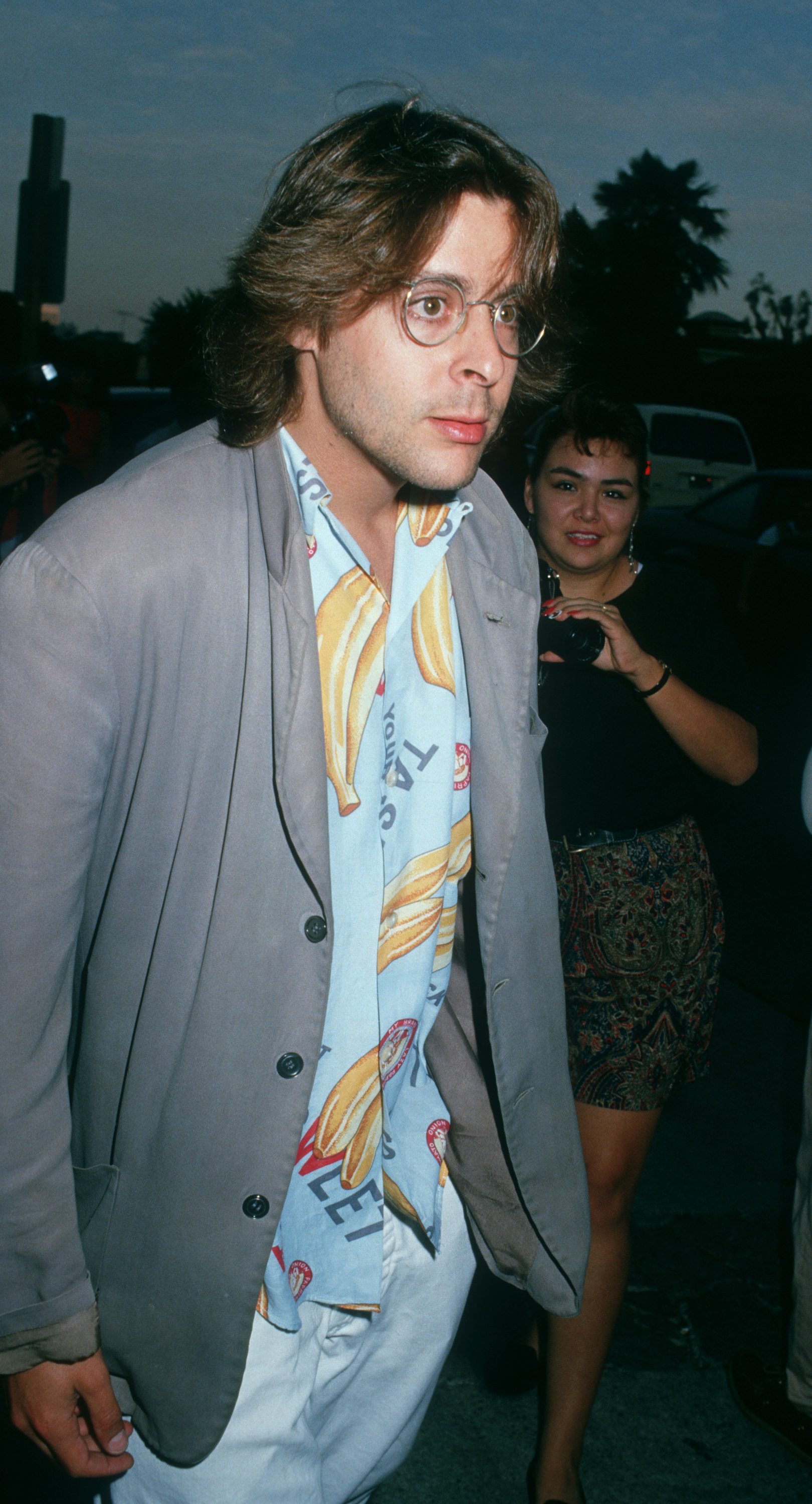Showcasing a casual late-eighties look in a banana-print shirt, wire-rimmed glasses, and a grey blazer, the actor arrives at the UA Coronet Theater in Westwood for the premiere of "Young Guns." | Source: Getty Images
