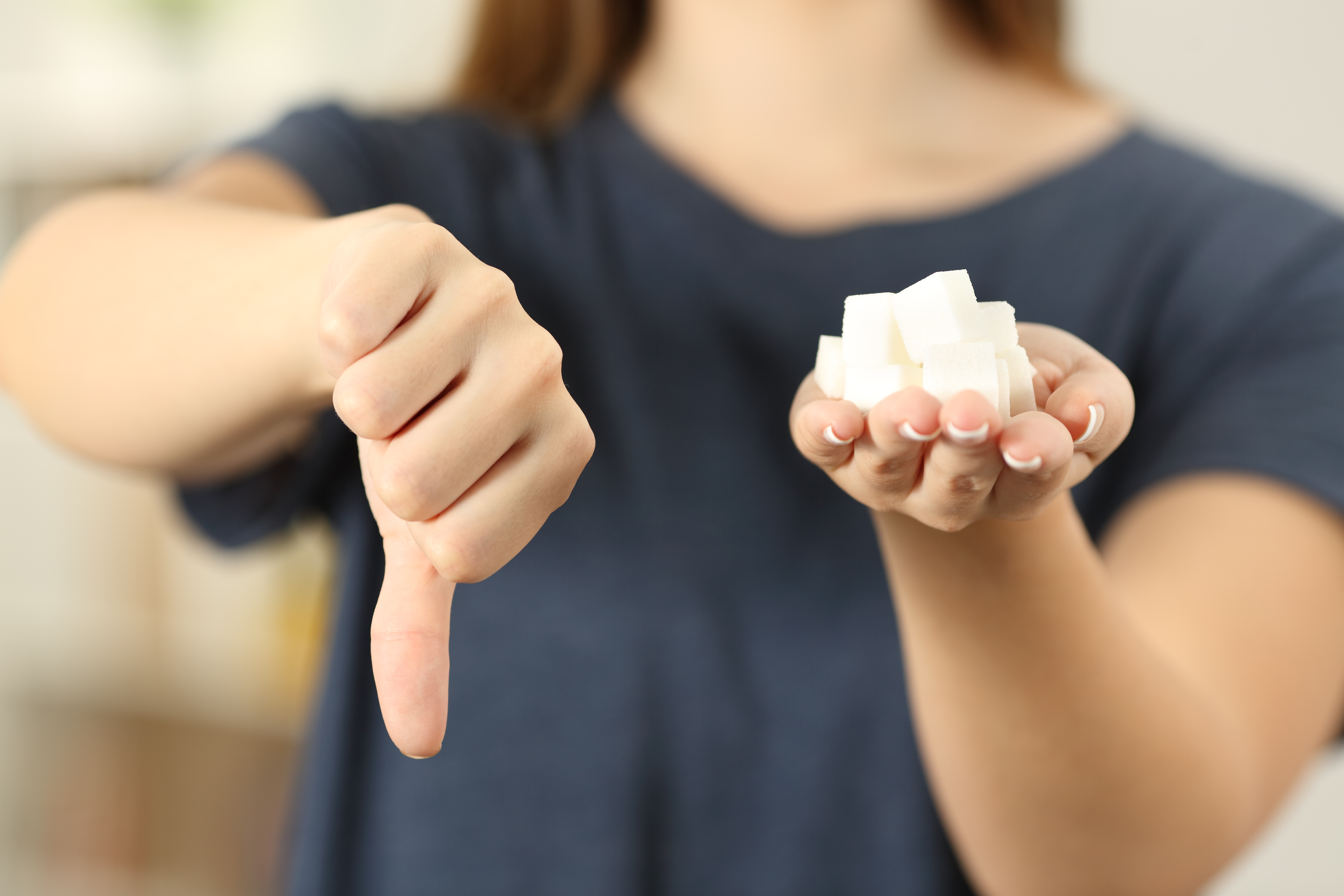 A woman holding sugar cubes in one hand while giving them the thumbs down with the other | Source: Shutterstock