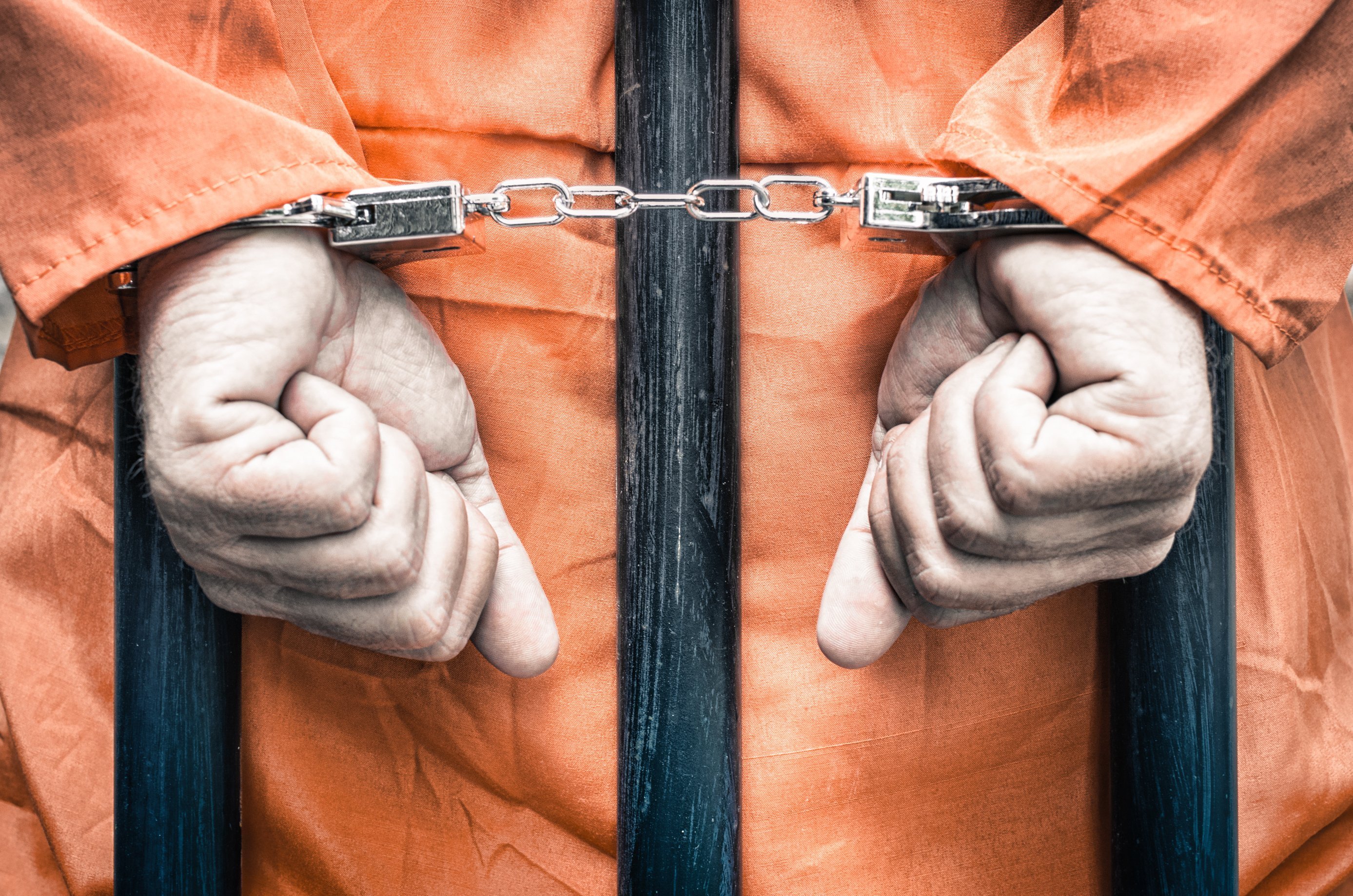Handcuffed prisoner behind the bars of a prison. | Source: Shutterstock