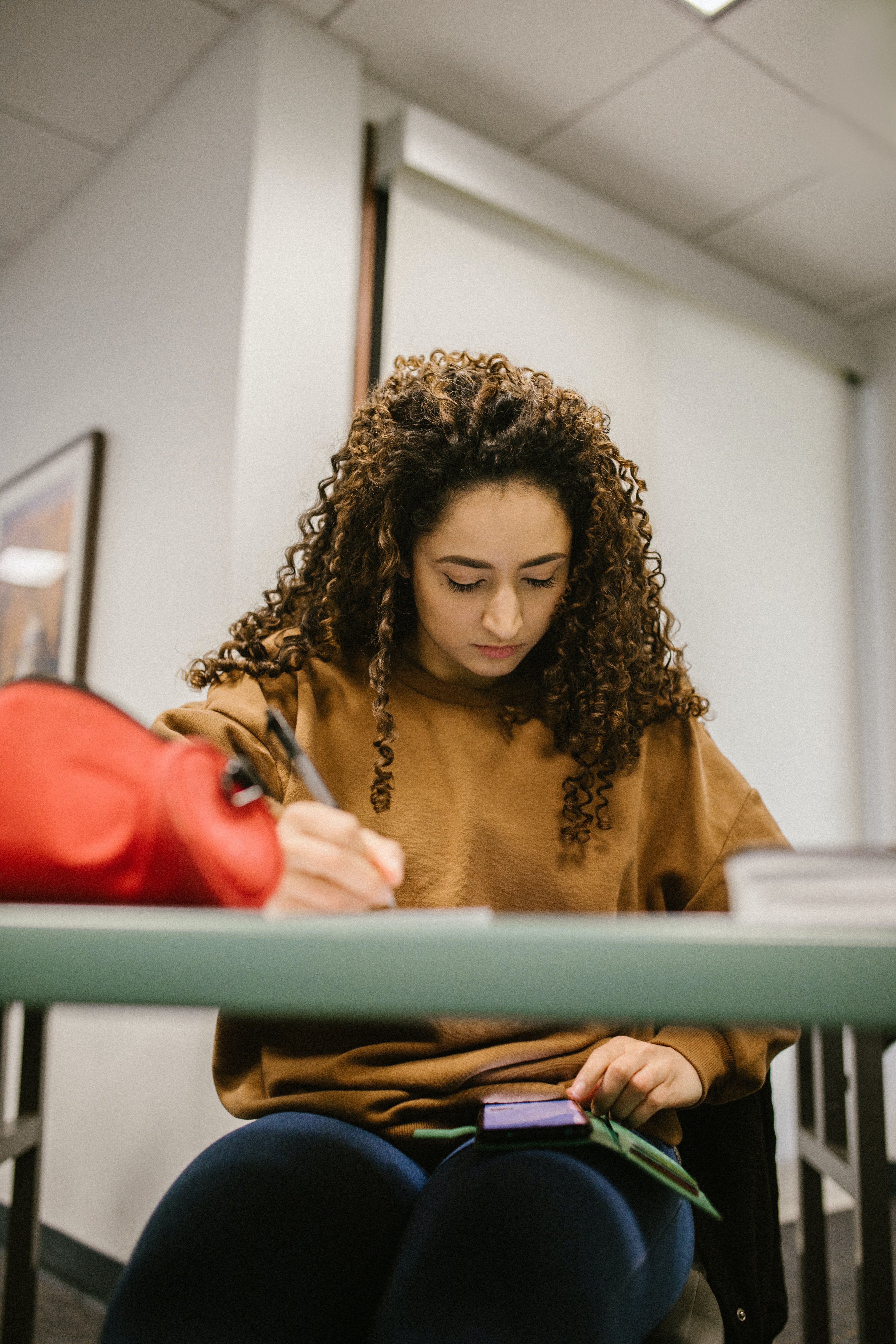 A female student writing a test with a phone on her lap. | Pexels/ RODNAE Productions 