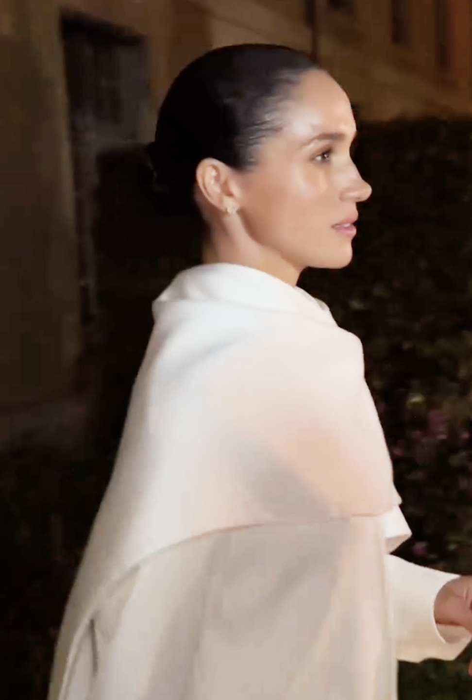 Meghan Markle, the Duchess of Sussex, is seen in a close-up at Paris Fashion Week, wearing a refined white ensemble. Her sleek bun and composed expression capture a moment of quiet confidence amid the excitement of the event.