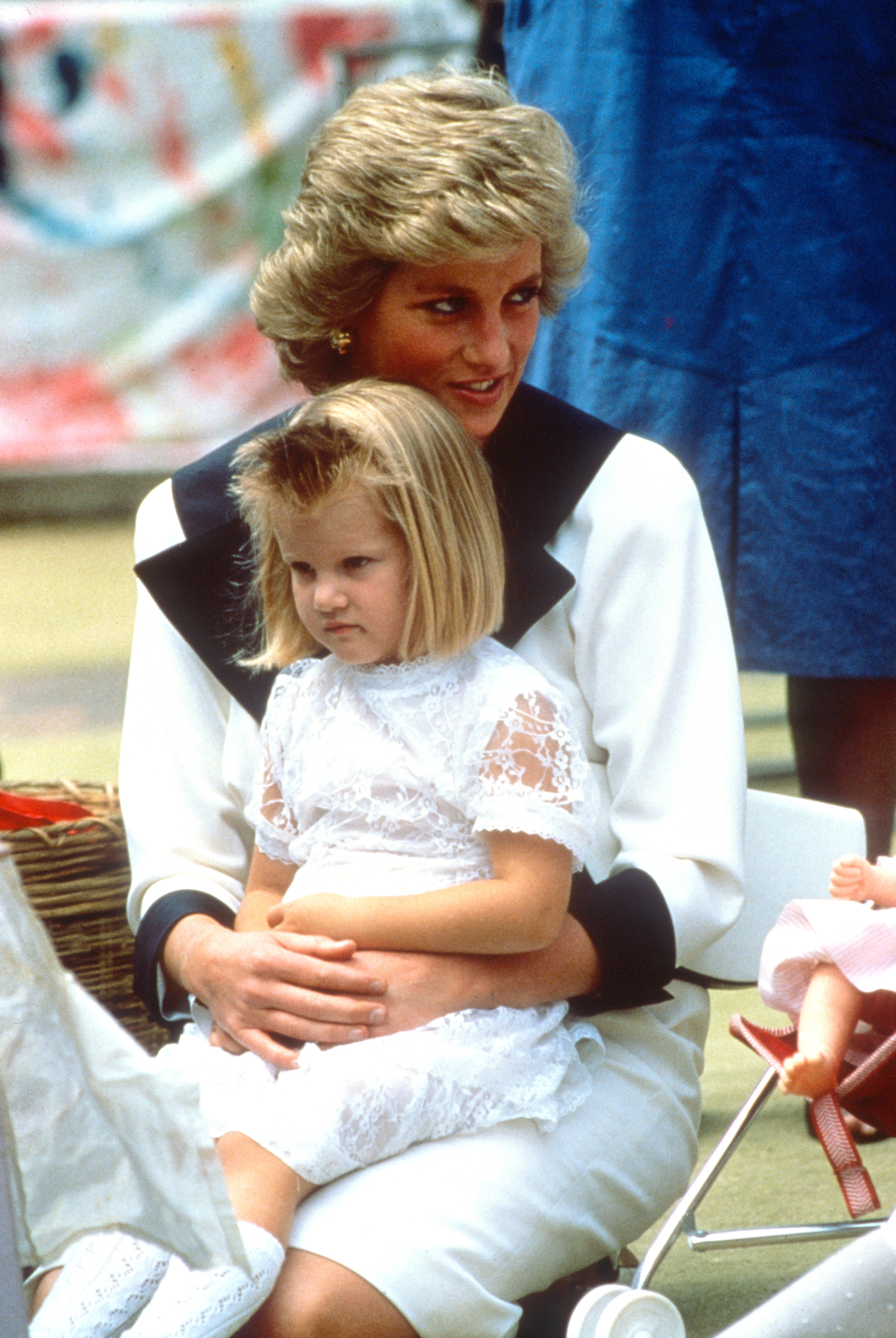 Diana, Princess of Wales, wearing a white dress with a navy blue collar designed by Catherine Walker, sits with a little girl on her lap during a visit to a Dr Barnardo's Home on February 2, 1988. | Source: Getty Images