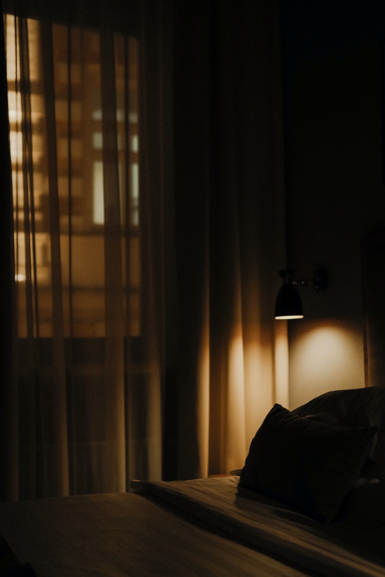 Una cama dentro de una habitación oscura con cortinas. | Foto: Pexels