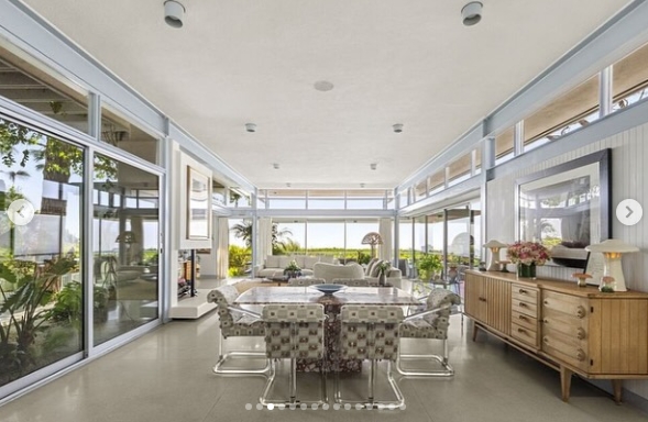 The dining area makes the most of the home's glass-heavy architecture, with windows wrapping around the space and bringing the surrounding greenery into view. A patterned dining set anchors the room, while warm wood cabinetry and carefully placed decor soften the clean lines and pale finishes. | Source: Instagram/jparkerstanton