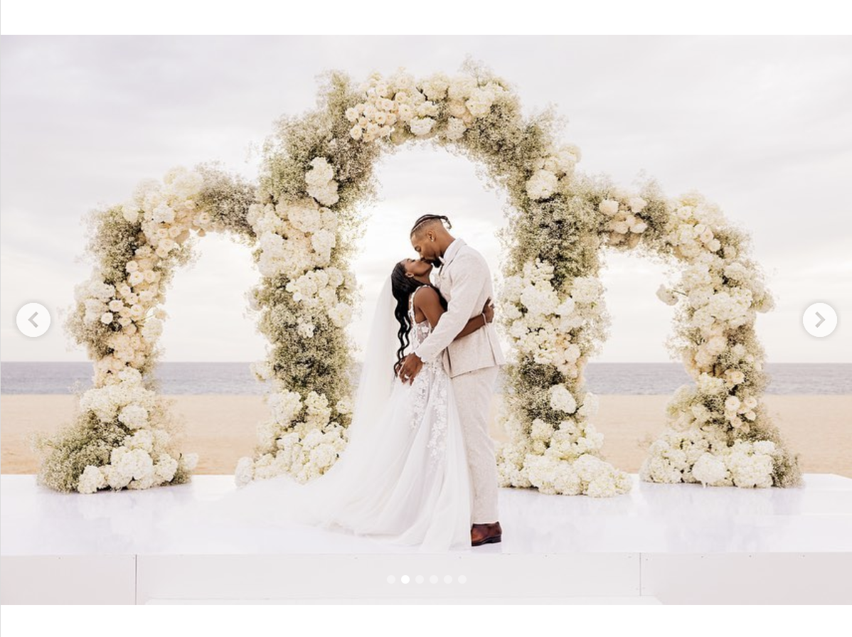 Simone Biles and Jonathan Owens share a kiss under a floral arch on their wedding day, as seen in a post dated May 9, 2023 | Source: Instagram/simonebiles