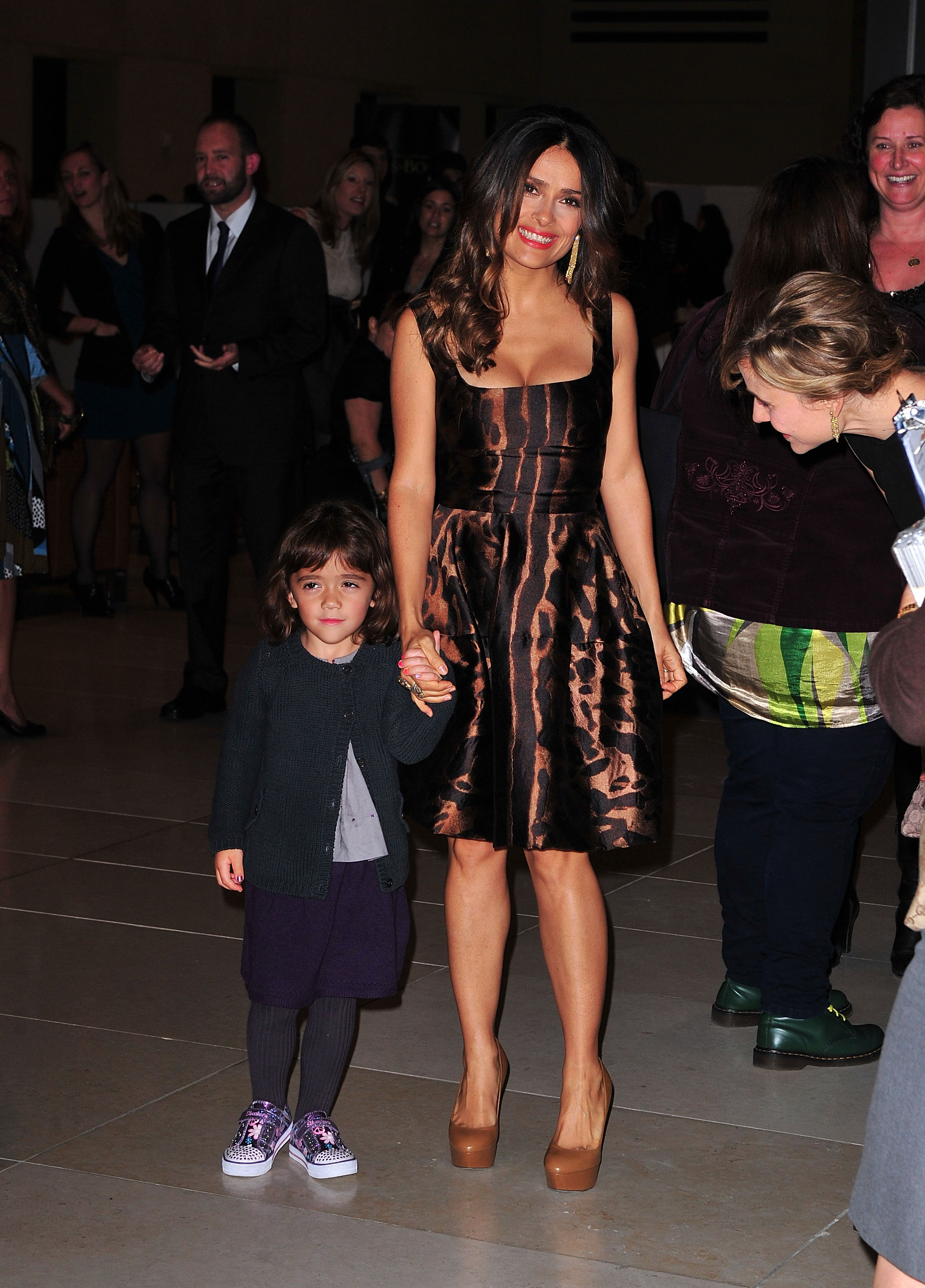 At the New York screening of "Puss in Boots," Salma Hayek and young Valentina Pinault take to the red carpet hand-in-hand. Salma stuns in an animal-print dress and towering nude heels, while Valentina, dressed in a cozy cardigan, purple skirt, and printed sneakers, appears slightly bashful next to her confident mom.