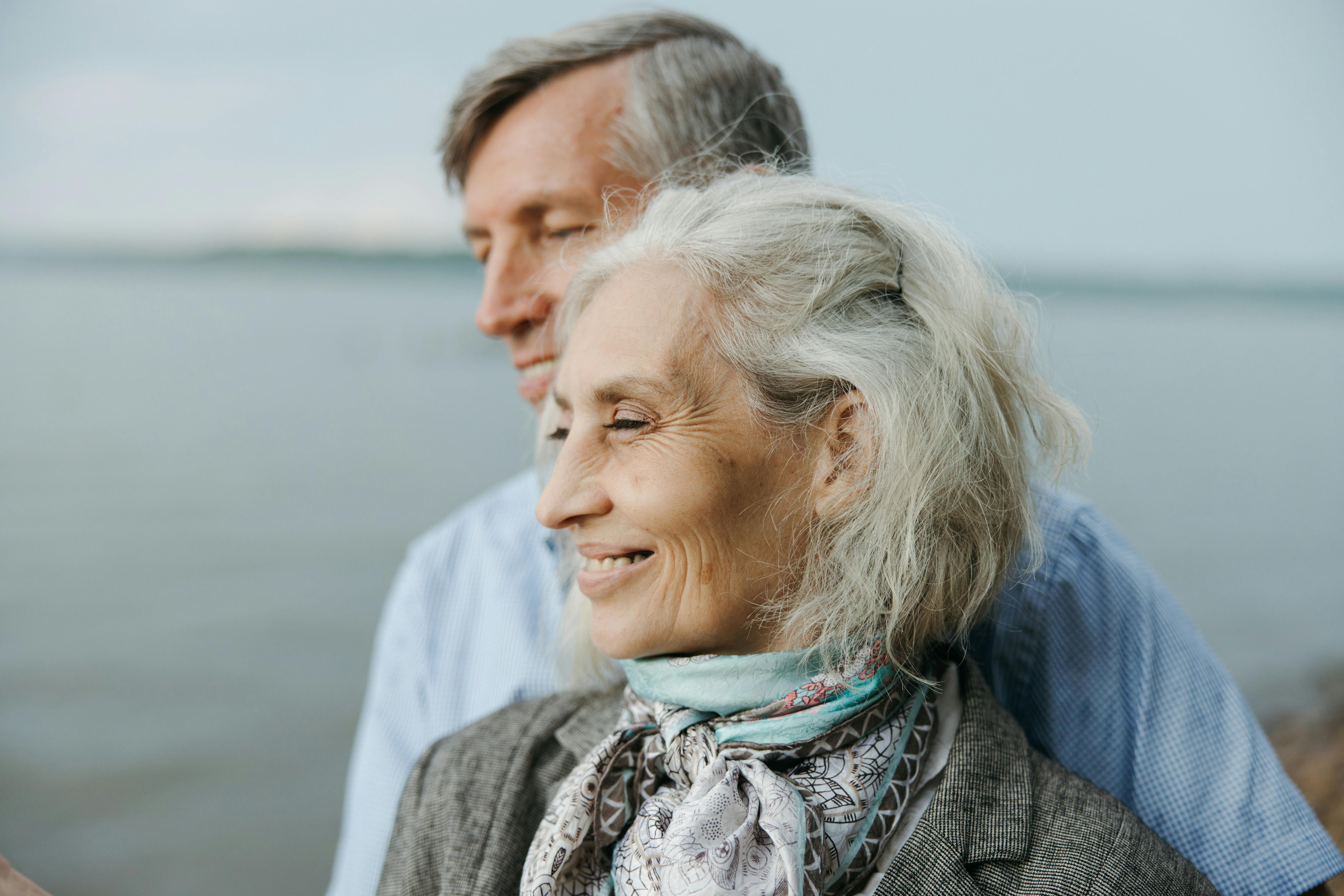 An older couple smiles while standing together by the water. | Source: Pexels