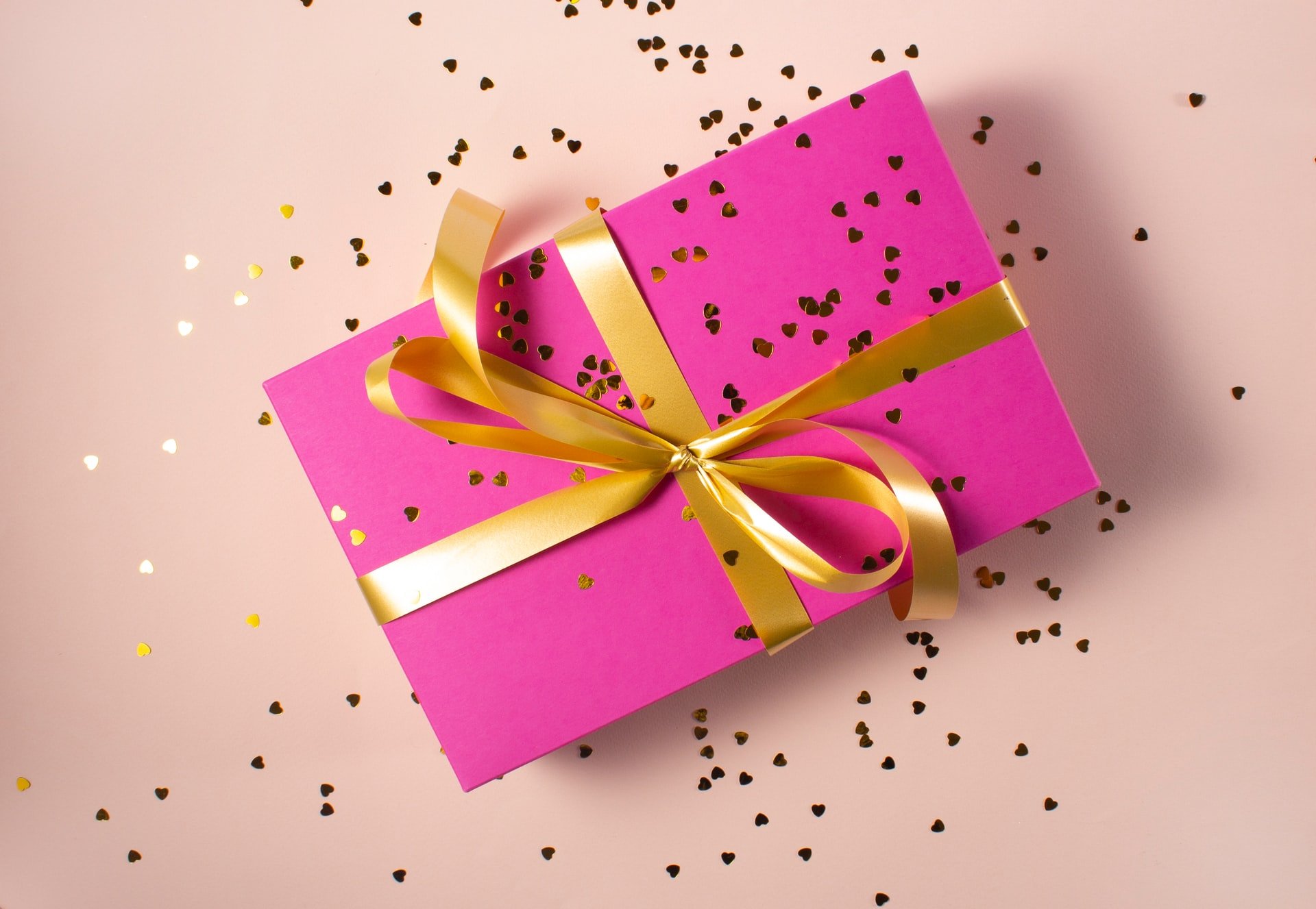 Gift wrapped in pink sheet with golden ribbon | Source: Unsplash