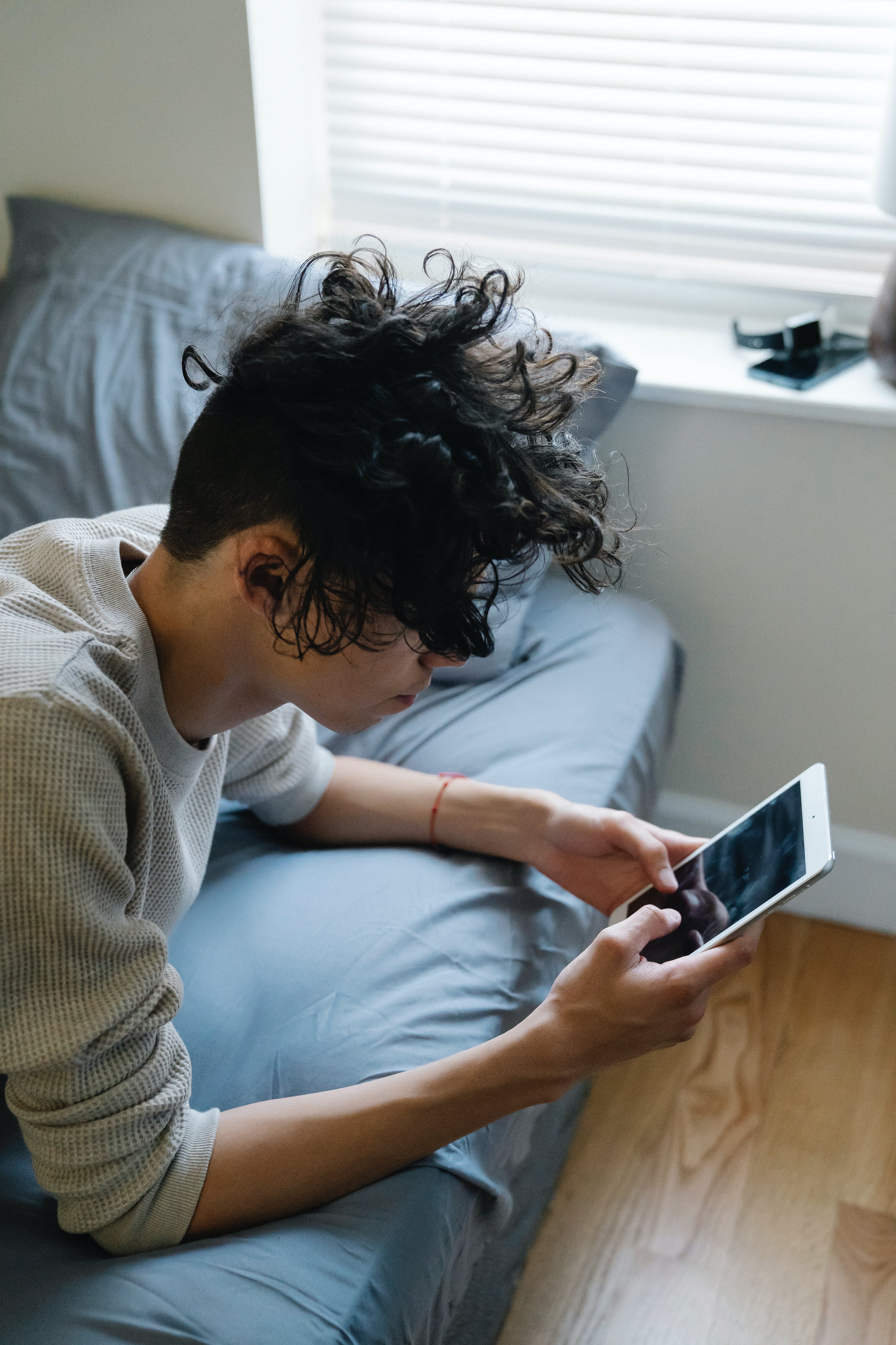 A young man texting on a phone while lying on a bed | Source: Pexels