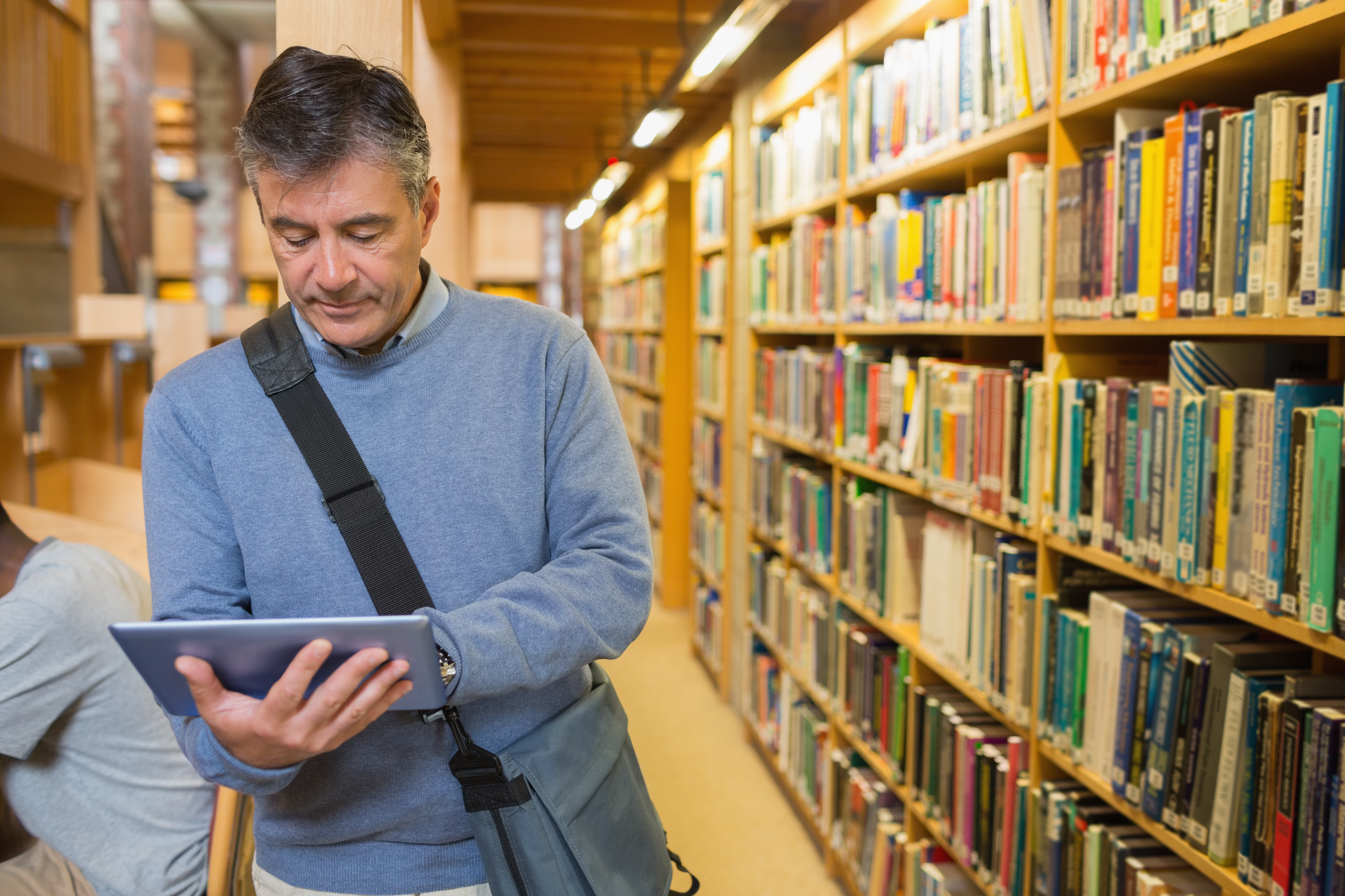 Hombre de cabello gris revisa tablet en biblioteca. | Foto: Getty Images
