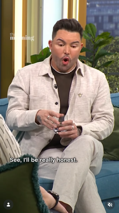 Norris mid-sentence on the "This Morning" sofa, wearing a cream linen jacket over a brown top and a pearl necklace, hands animated as he begins to open up about his cosmetic journey. | Source: Instagram/thismorning