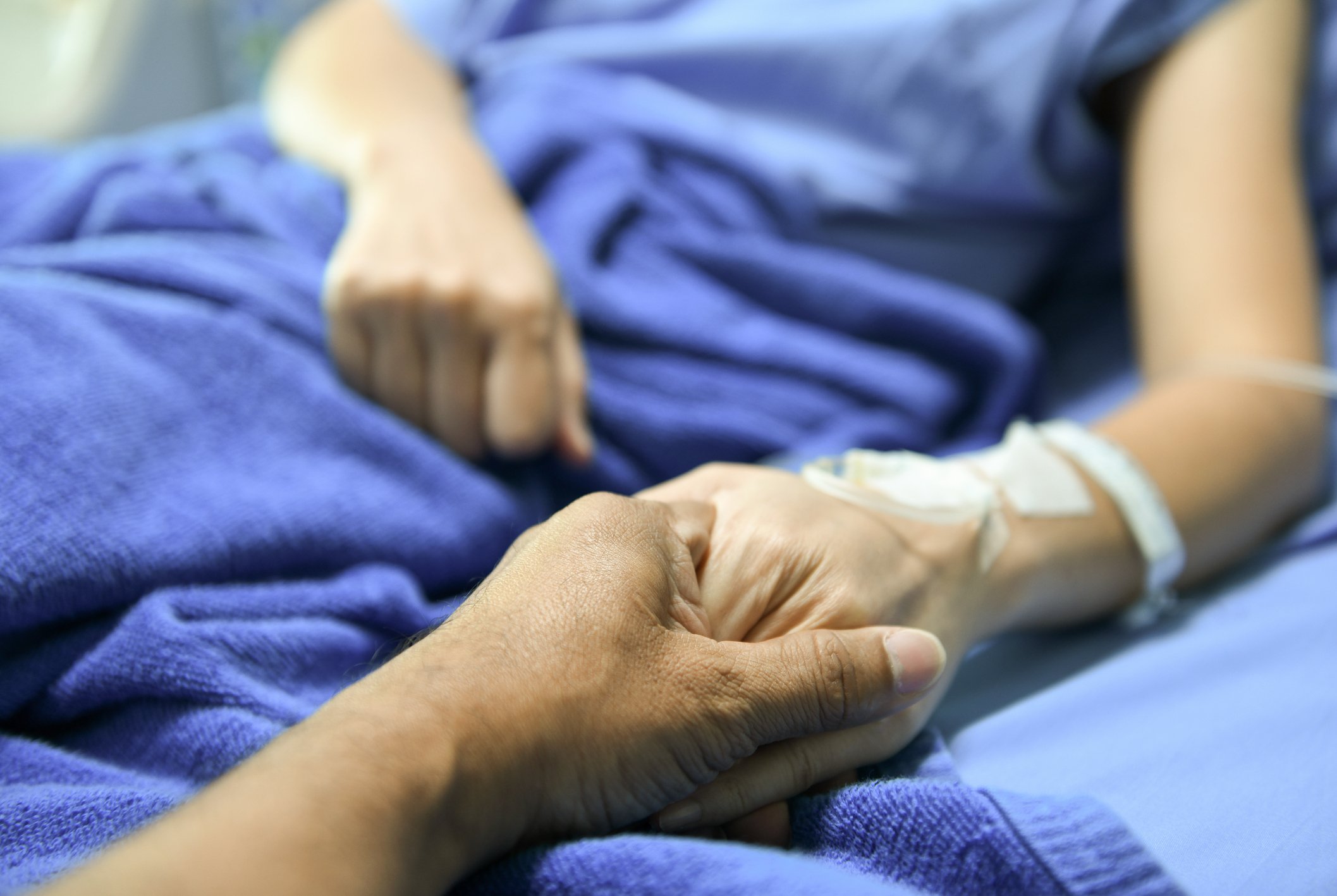 Hand des Mannes tröstet Patienten auf Bett I Quelle: Getty Images