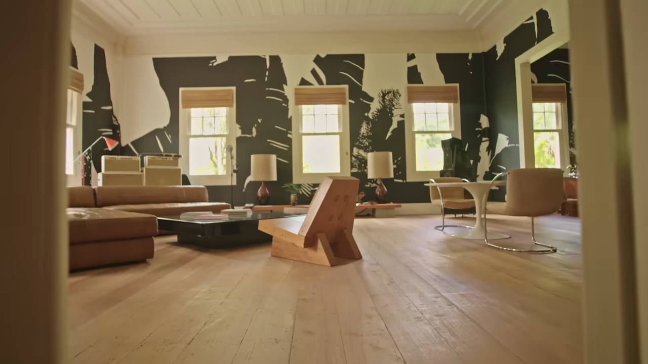 A wide look at the open-concept living room, designed with light wood floors, a modular leather sofa, and bold black-and-white botanical wallpaper. | Source: YouTube/@Archdigest