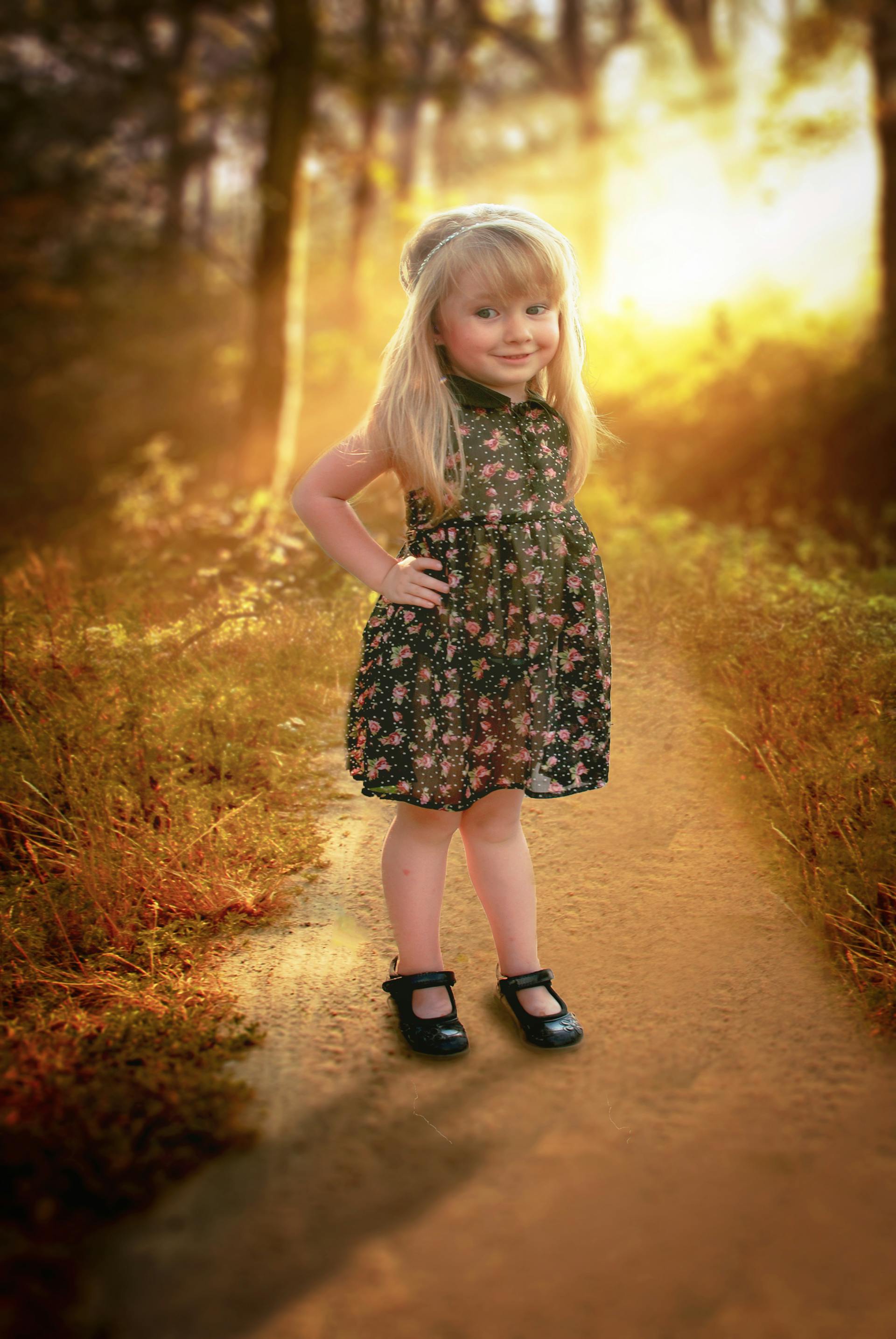 A happy little girl in a floral dress standing on a pathway | Source: Pexels