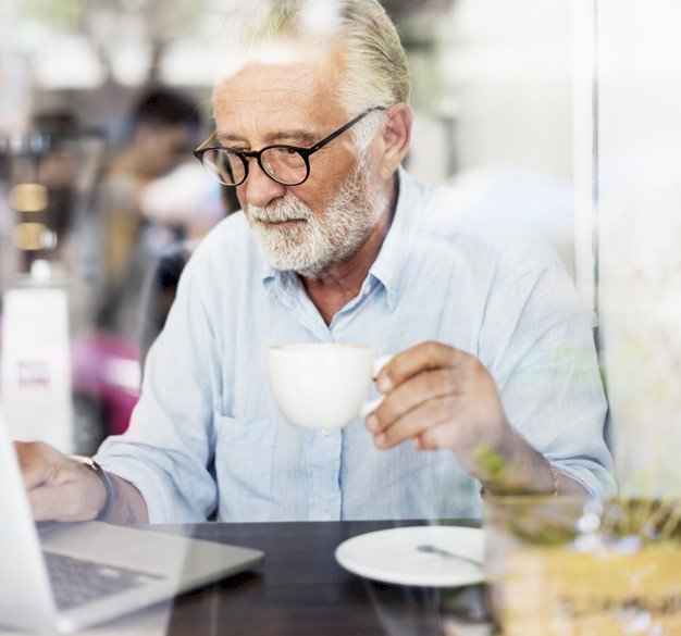 Old man working with a laptop and holding a cup | Source: Freepik