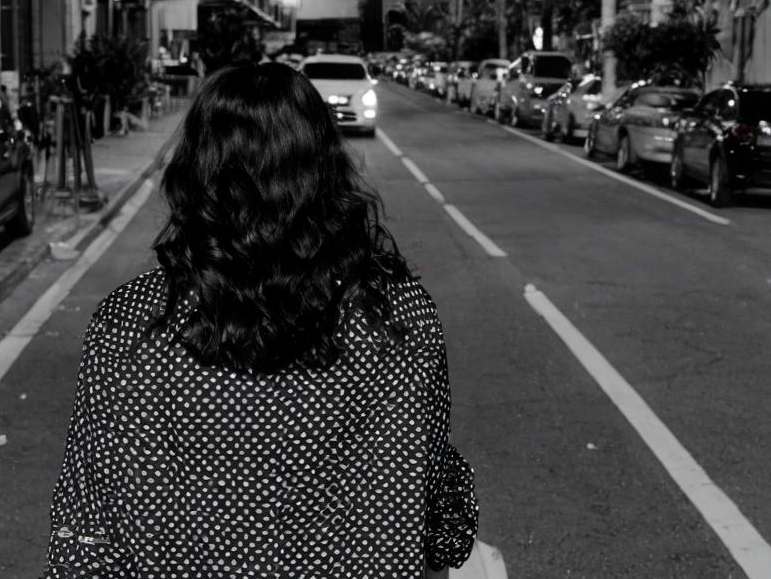 A woman walking away down a street at night | Source: Midjourney