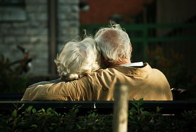 Pareja de ancianos abrazados mientras están sentados en una banquilla. | Foto: Wikimedia Commons