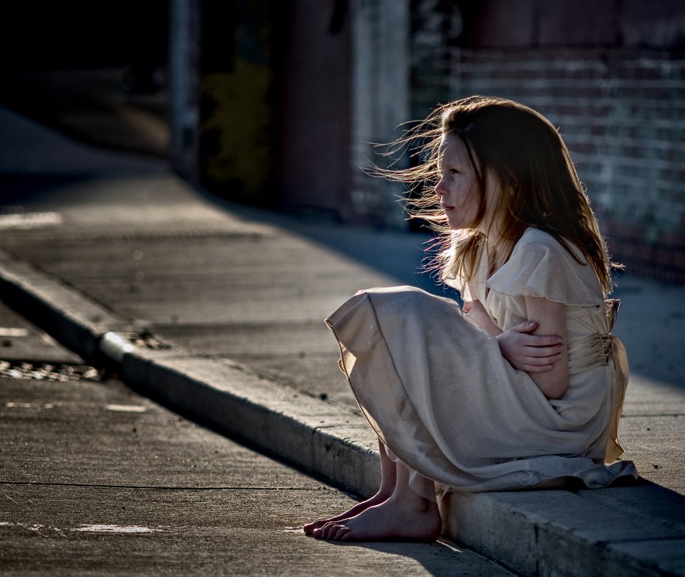 Une fille assise sur le trottoir dans une robe sale.| Photo  : Shutterstock