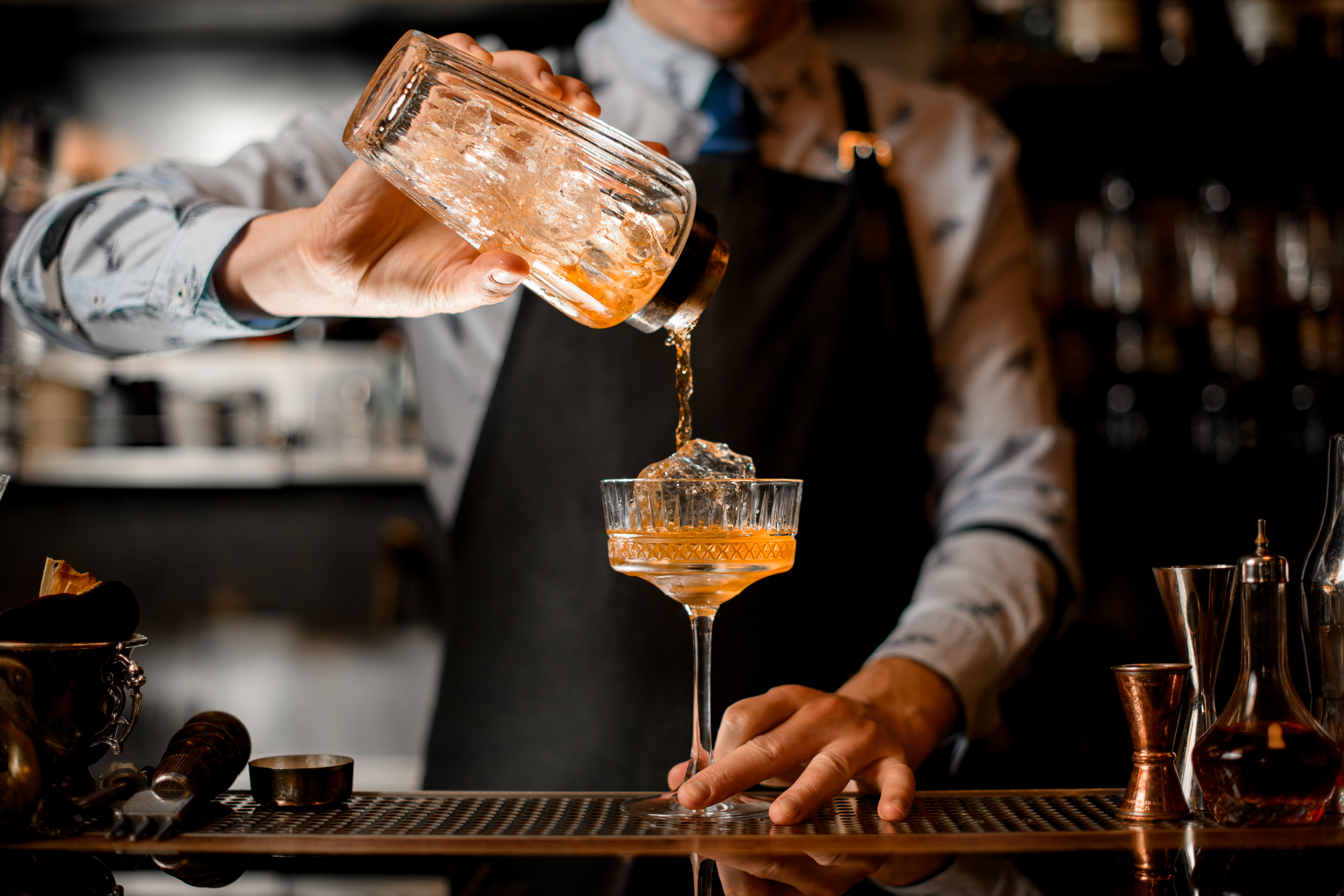 Barman gently pours finished cocktail from glass shaker into glass. | Source: Shutterstock