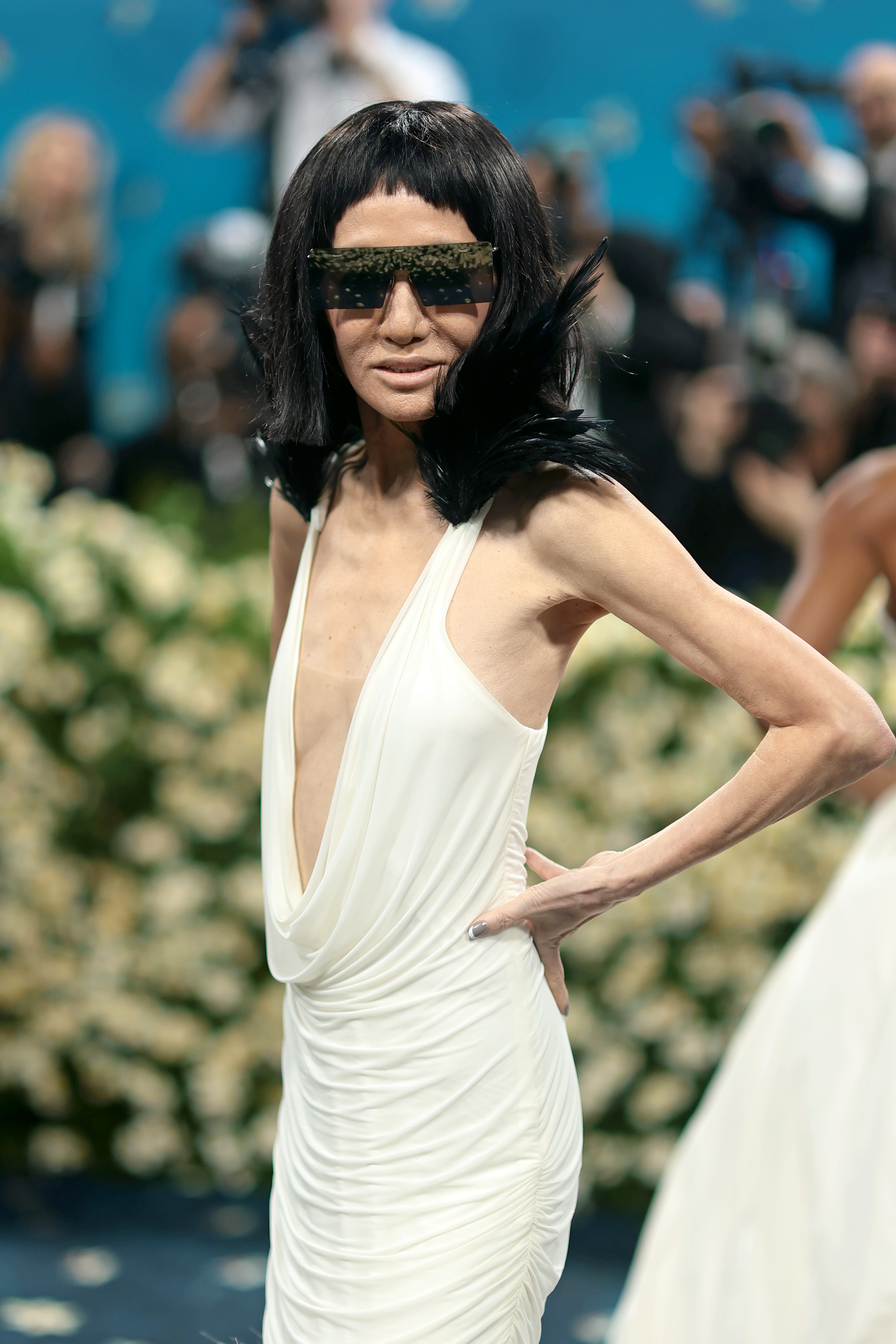 On the Met Gala red carpet, Vera Wang stuns in a plunging white draped gown. She completes the bold, futuristic look with oversized crystal-studded sunglasses and a black wig, commanding attention with her fearless fashion statement.