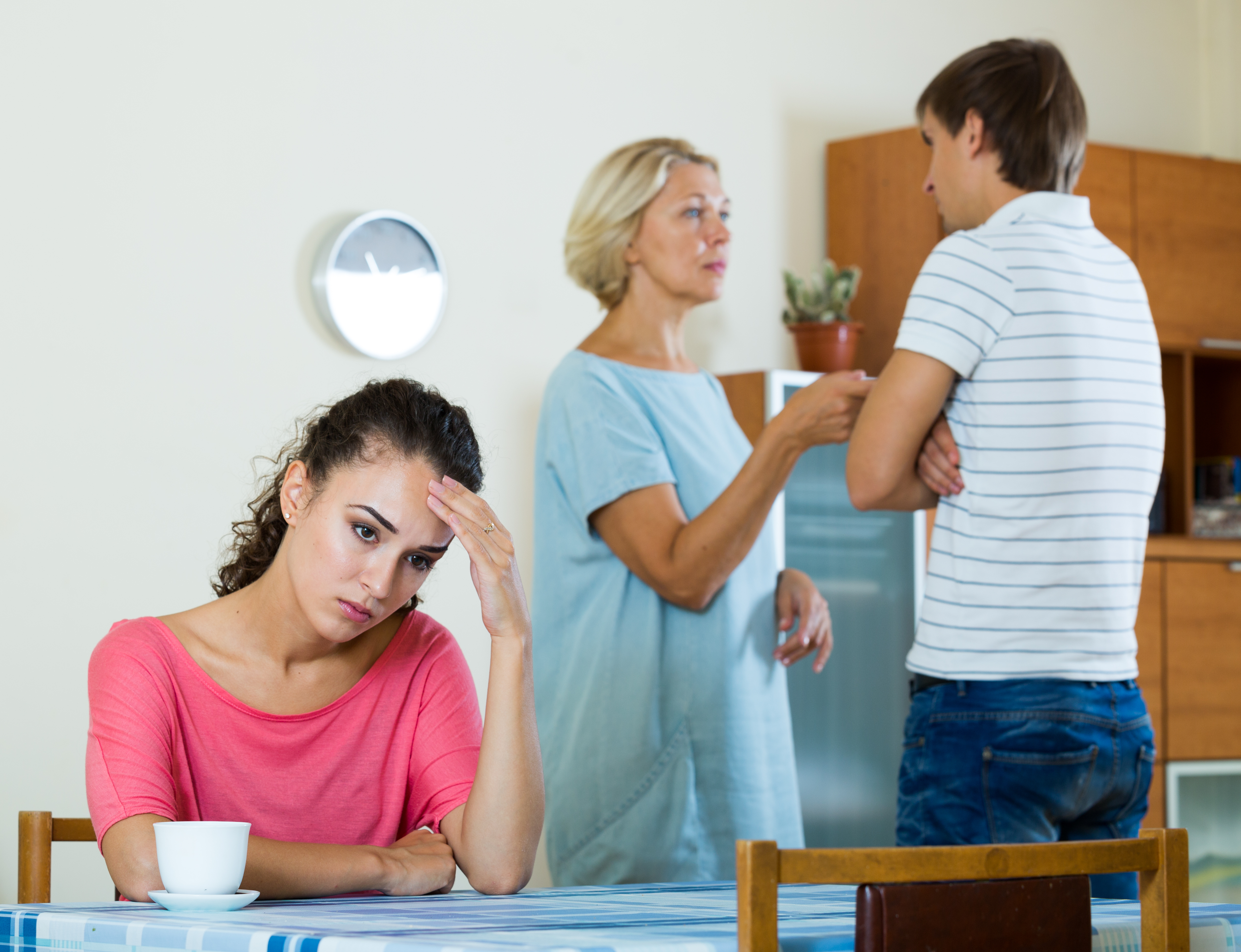 An upset young woman with her husband and mother arguing in the background | Source: Shutterstock