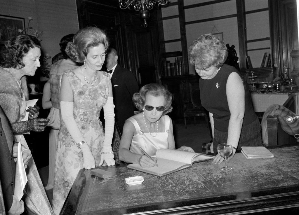 La reina María José de Italia firma el libro de visitas en la Salle Gaveau, a su derecha, la reina Fabiola de Bélgica. | Foto: Getty Images.