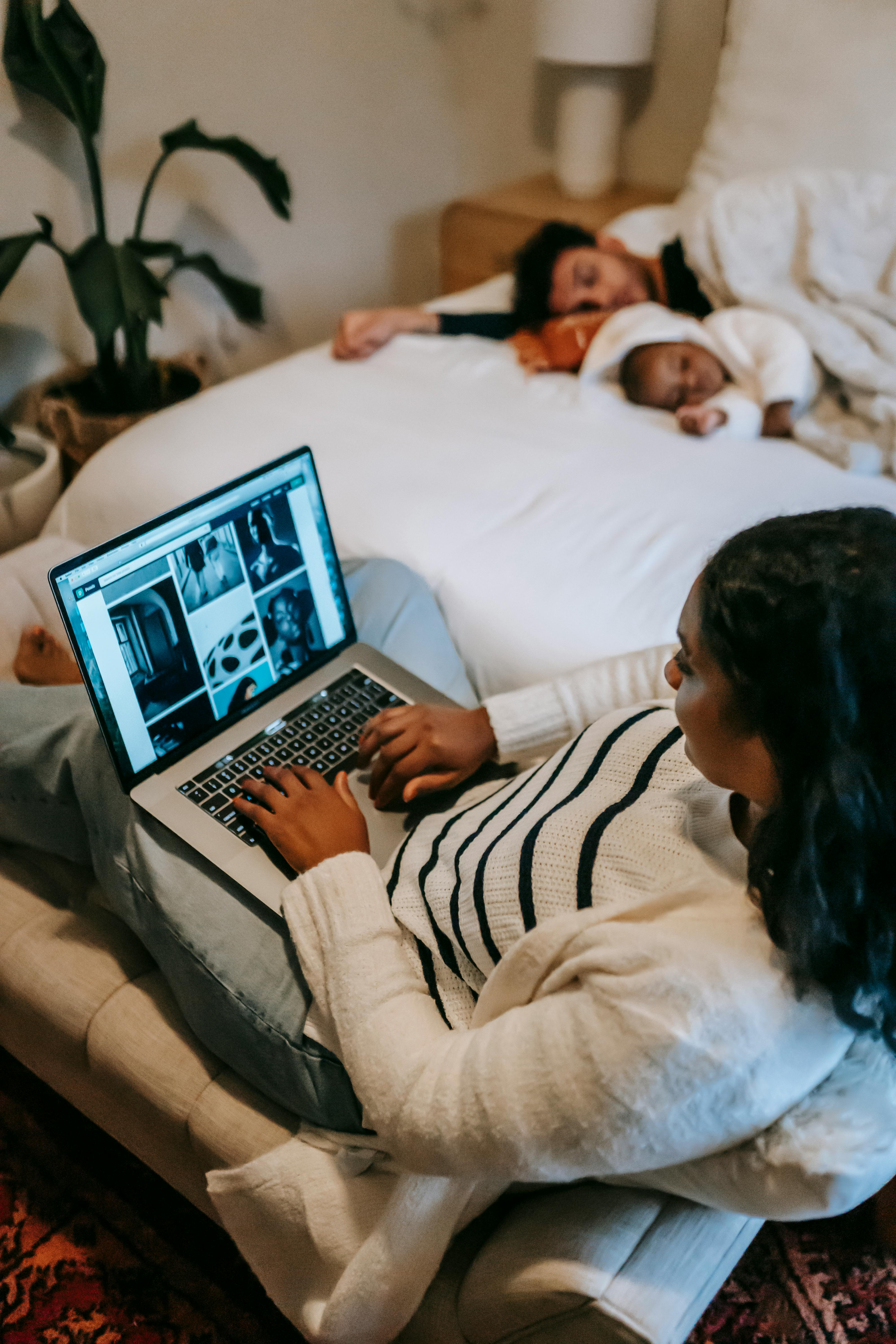 A woman on her laptop and her family sleeping on the bed | Source: Pexels