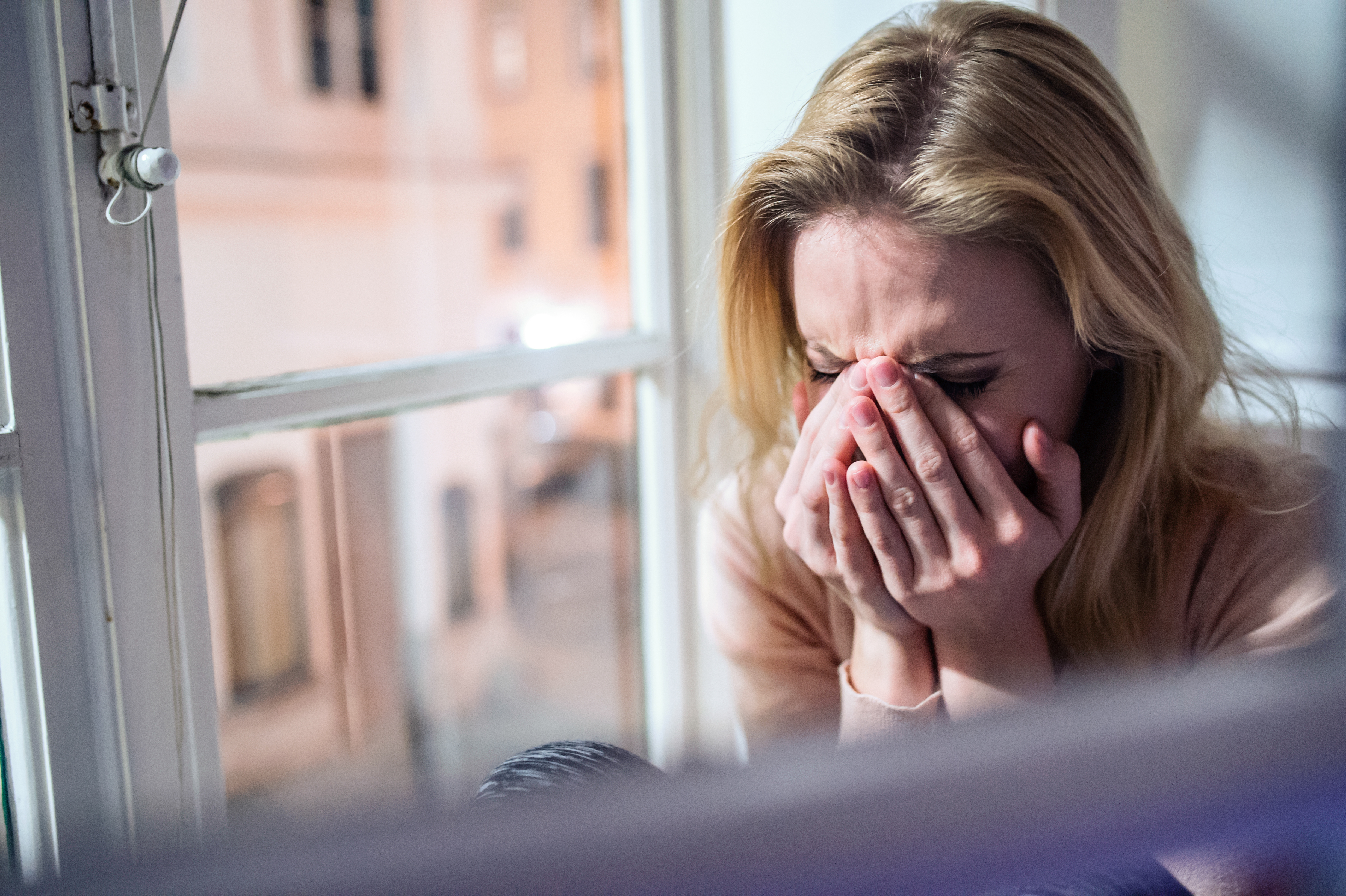 Woman sitting on windowsill, looking out of window, crying. | Source: Shutterstock