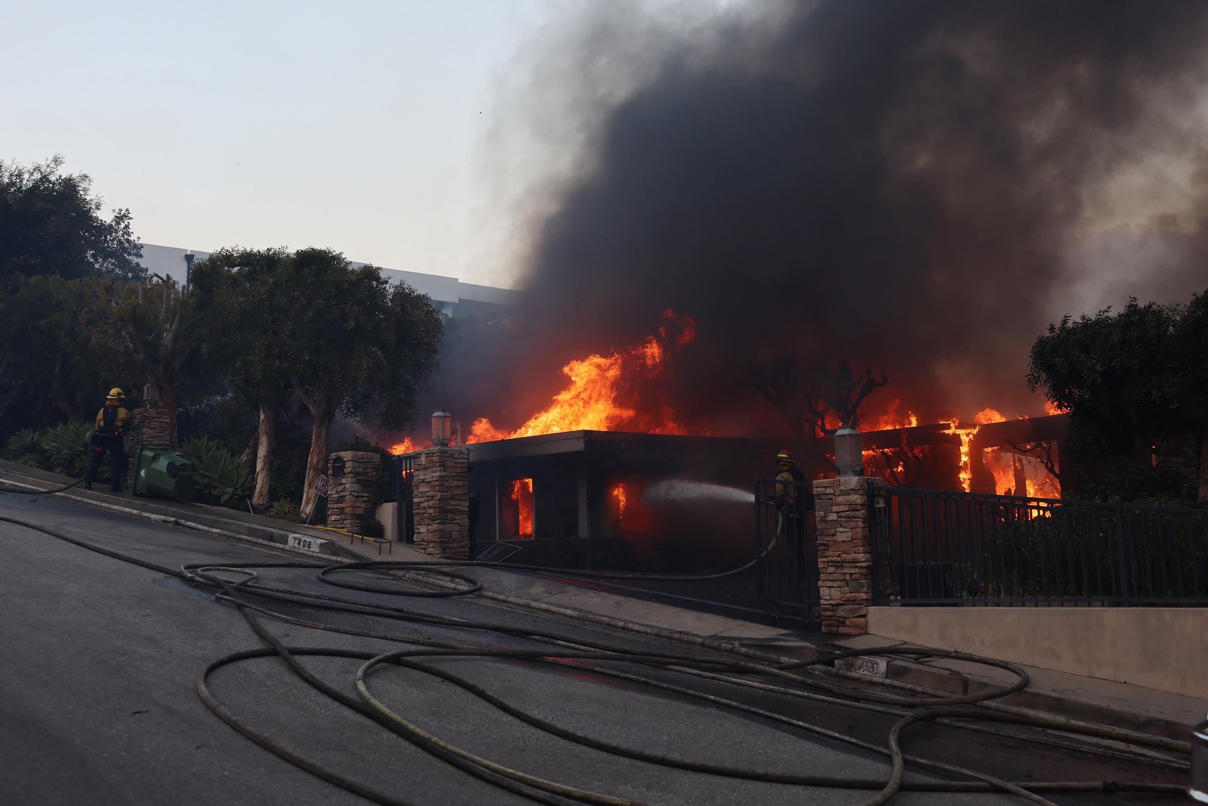 A firefighter dousing a house engulfed by flames from the Palisades fire in Palisades, California on January 7, 2025. | Source: Getty Images