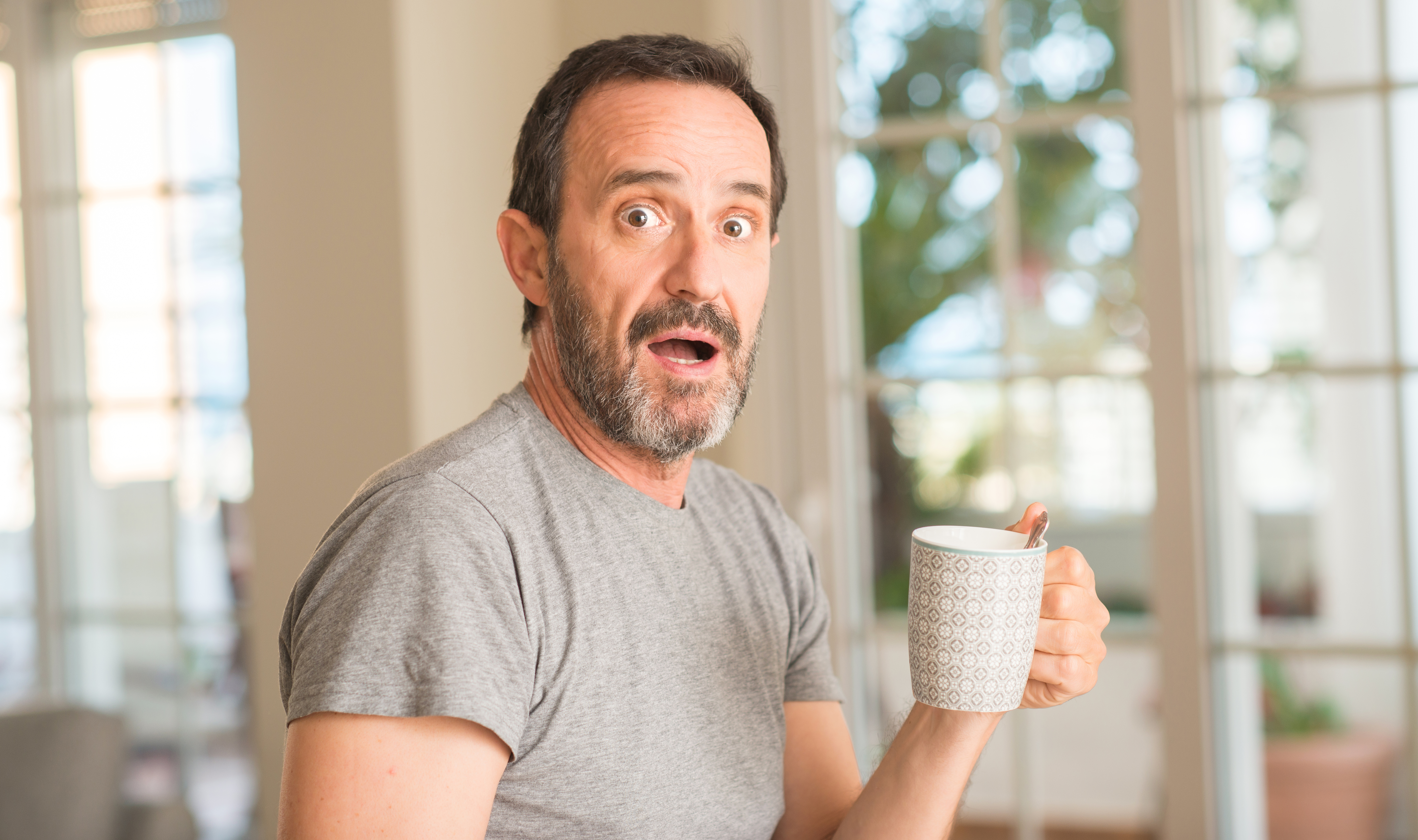 Middle age man drinking coffee in a cup scared in shock with a surprise face, afraid and excited with fear expression | Source: Getty Images