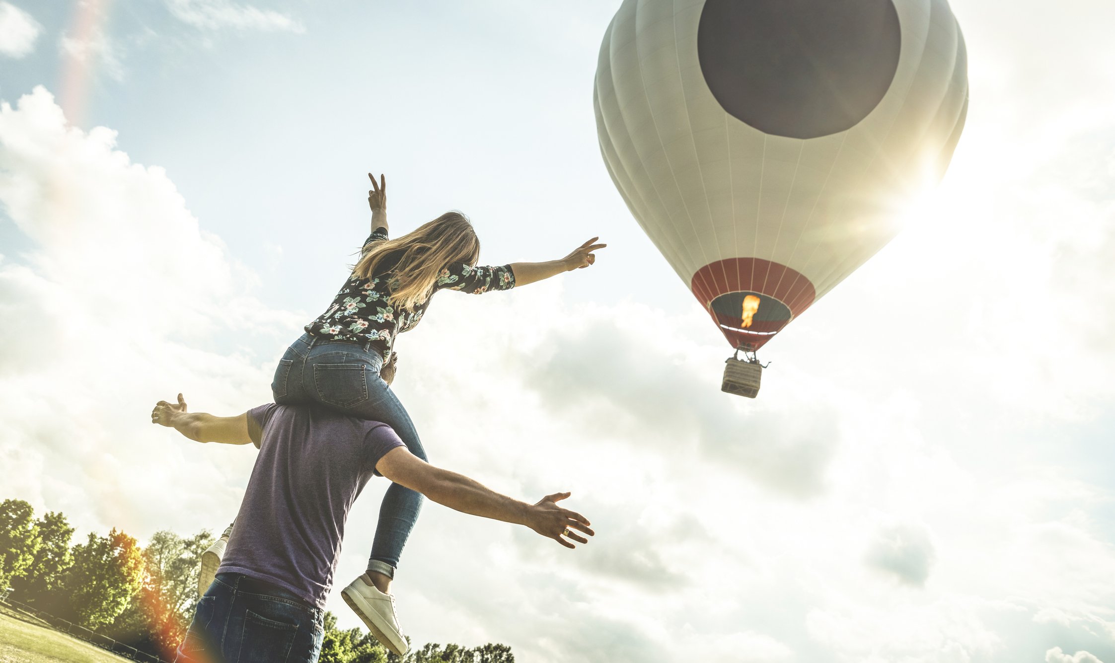 Photo of a couple having fun while a hot air ballon flying in the sky. | Photo: Getty Images