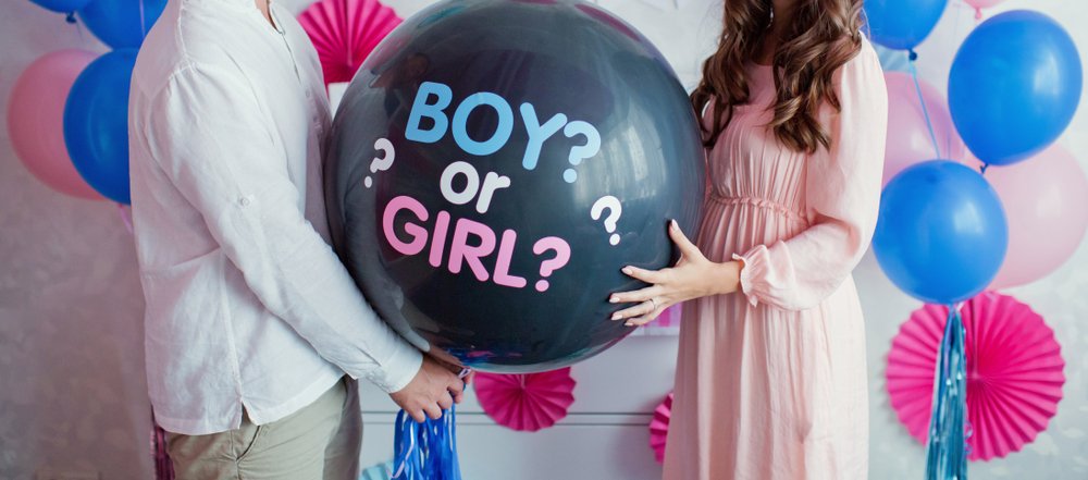 Expecting parents holding a black balloon with "boy or girl?" in gender reveal party. | Photo: Shutterstock.