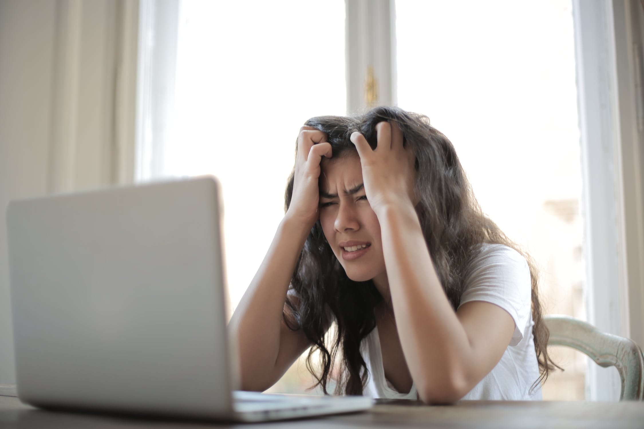 Mujer joven hace un gesto de desesperación frenta a su computadora portátil. | Foto: Pexels