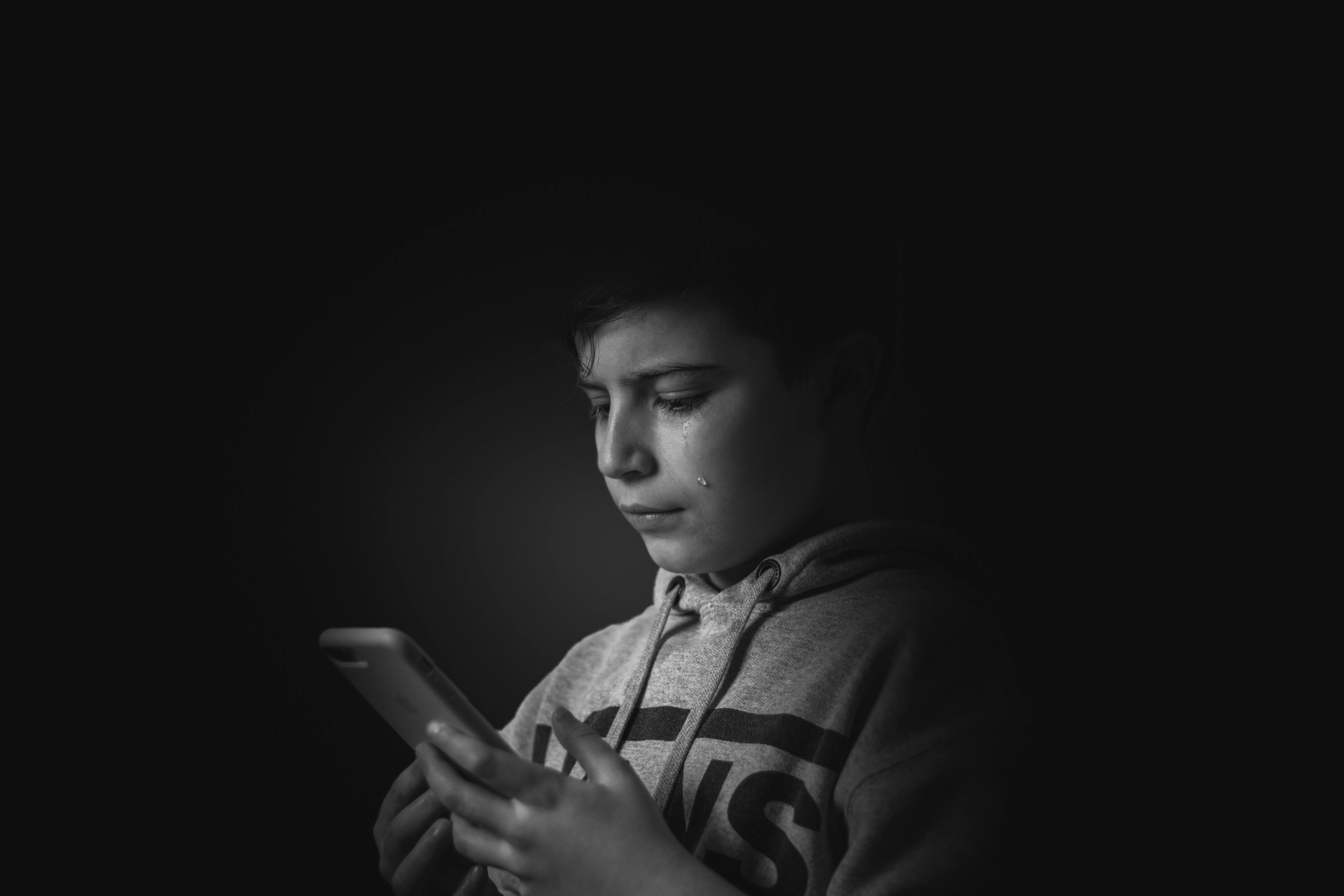 A crying boy looking at his phone | Source: Pexels