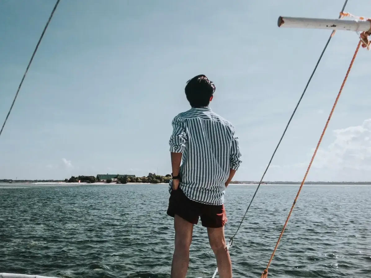 A man peers overboard towards a small offshore island | Source: Pexels